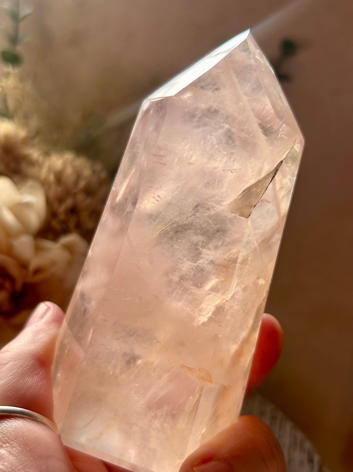 Pink crystal held in a hand with a blurred natural background