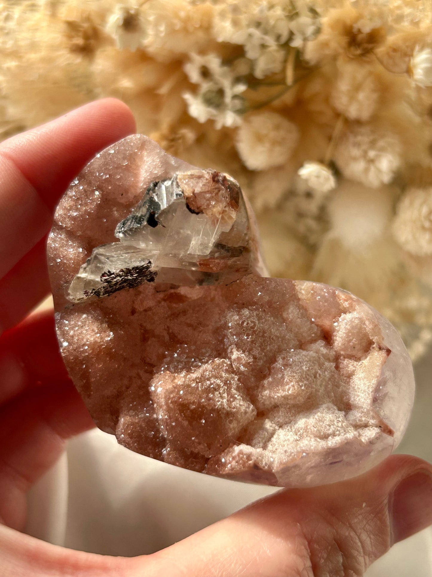 Blush pink druzy Amethyst heart with exposed mineral inclusions and raw crystal clarity, held in hand with dried floral background
