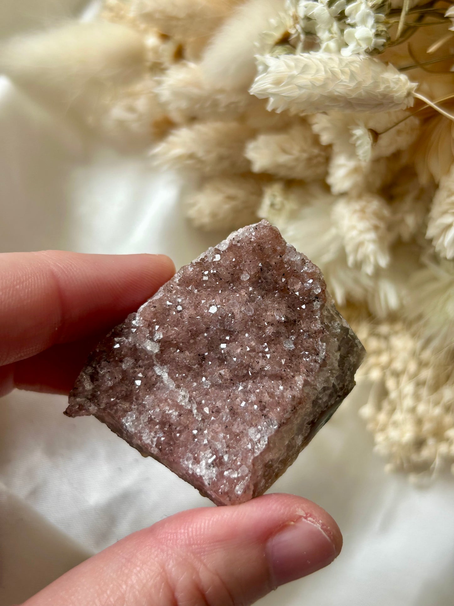 Small druzy rainbow sugar geode clusters with pastel tones and glittering crystal surfaces, displayed on ivory silk with cream dried flowers in the background.