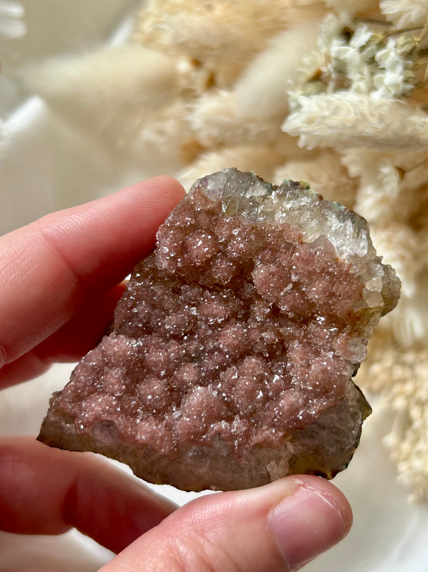 Small druzy rainbow sugar geode clusters with pastel tones and glittering crystal surfaces, displayed on ivory silk with cream dried flowers in the background.