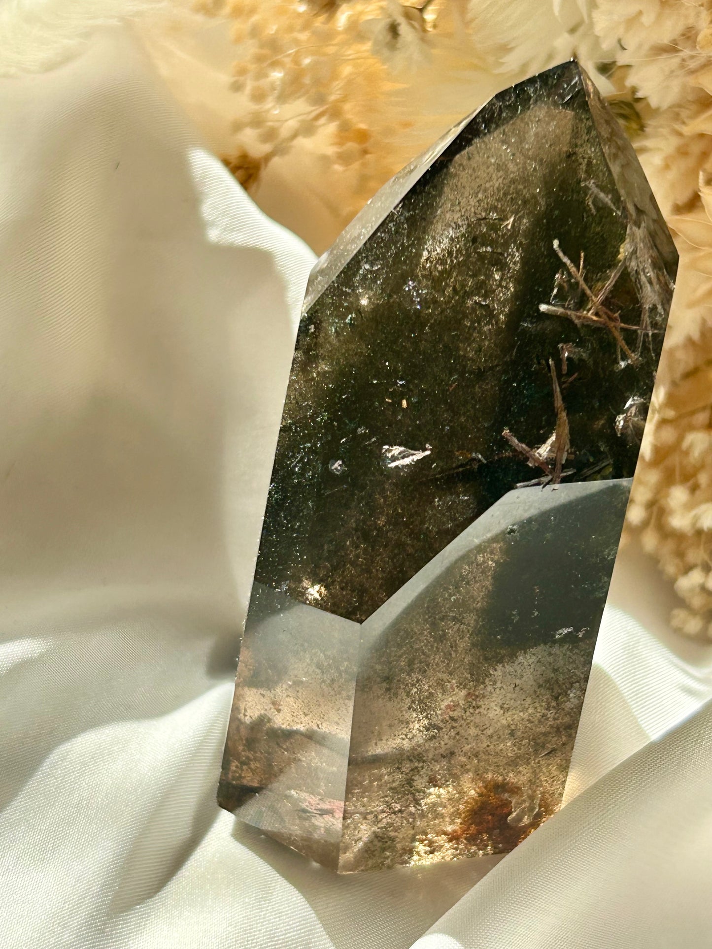 Smoky Quartz tower with chlorite inclusions and rutile resting on ivory satin, catching golden sunlight with earthy internal reflections.