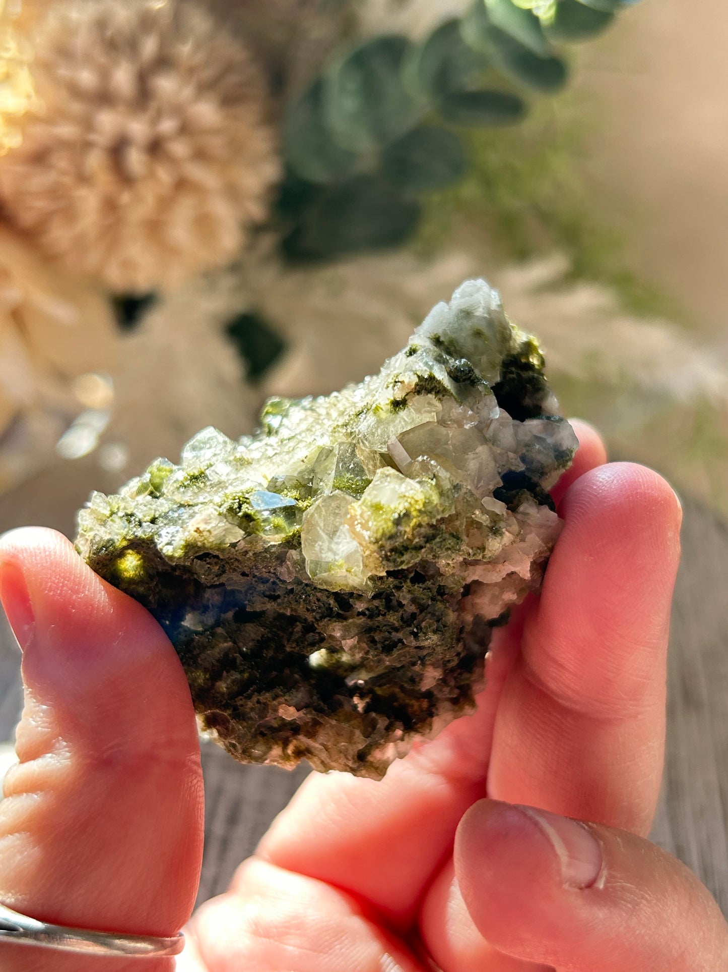 Person holding a piece of green crystal rock with blurred natural background