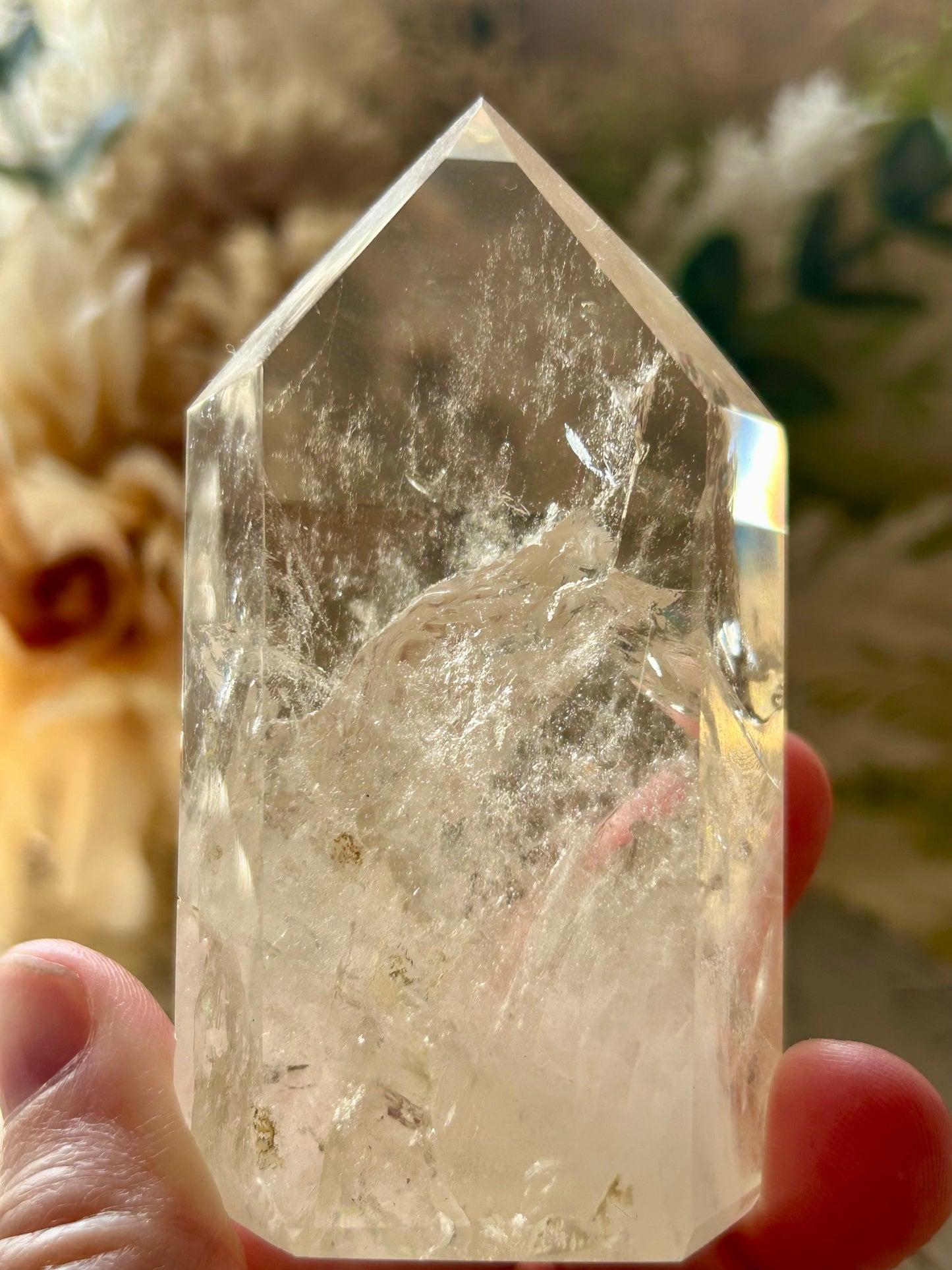 Clear crystal held by a hand with a blurred natural background