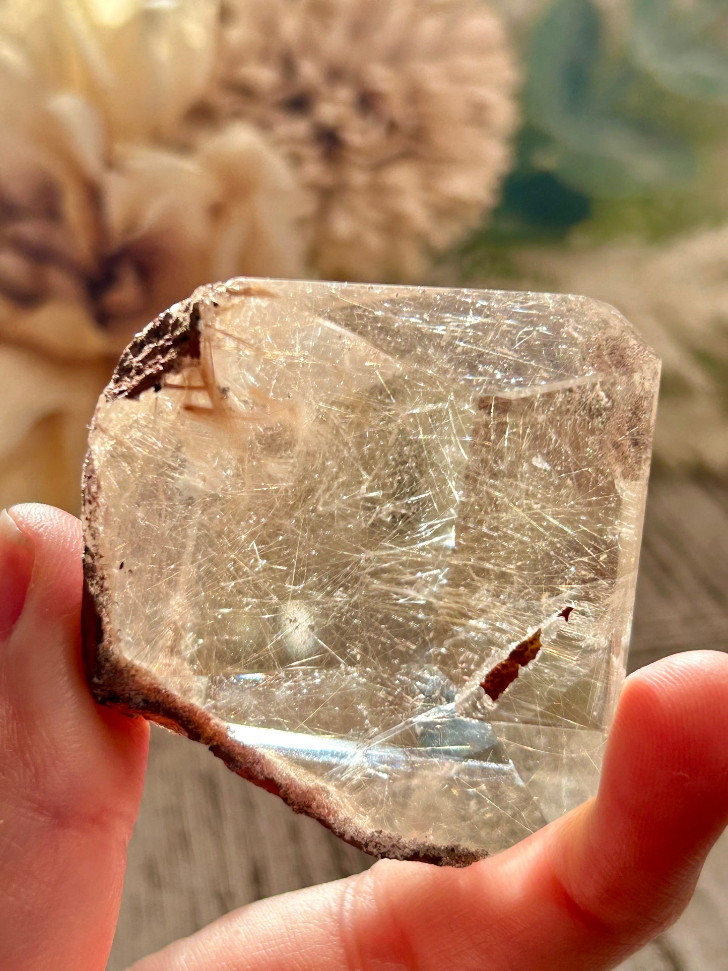 Clear crystal held between fingers with a blurred natural background