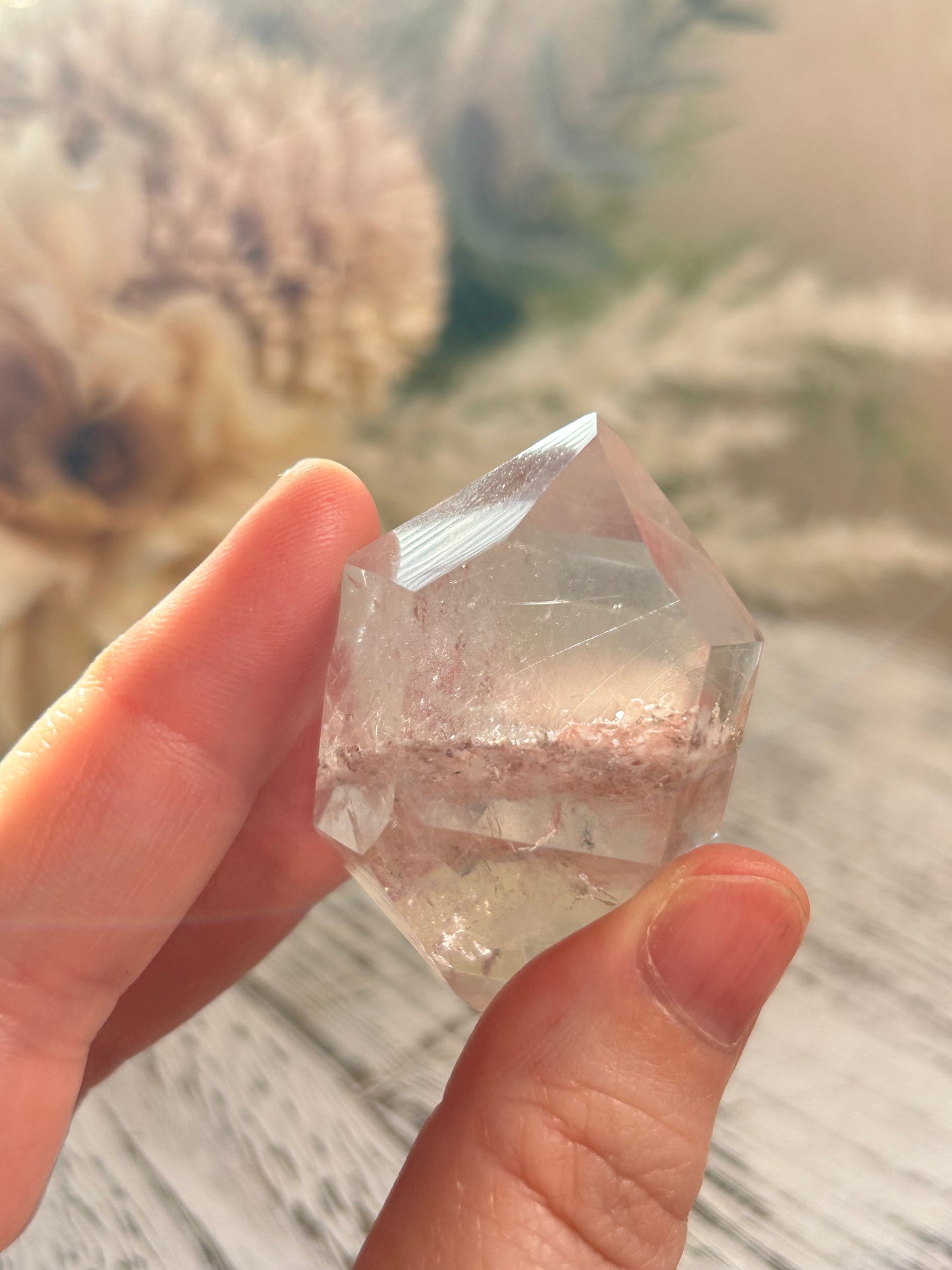 Hand holding a clear crystal with a blurred natural background