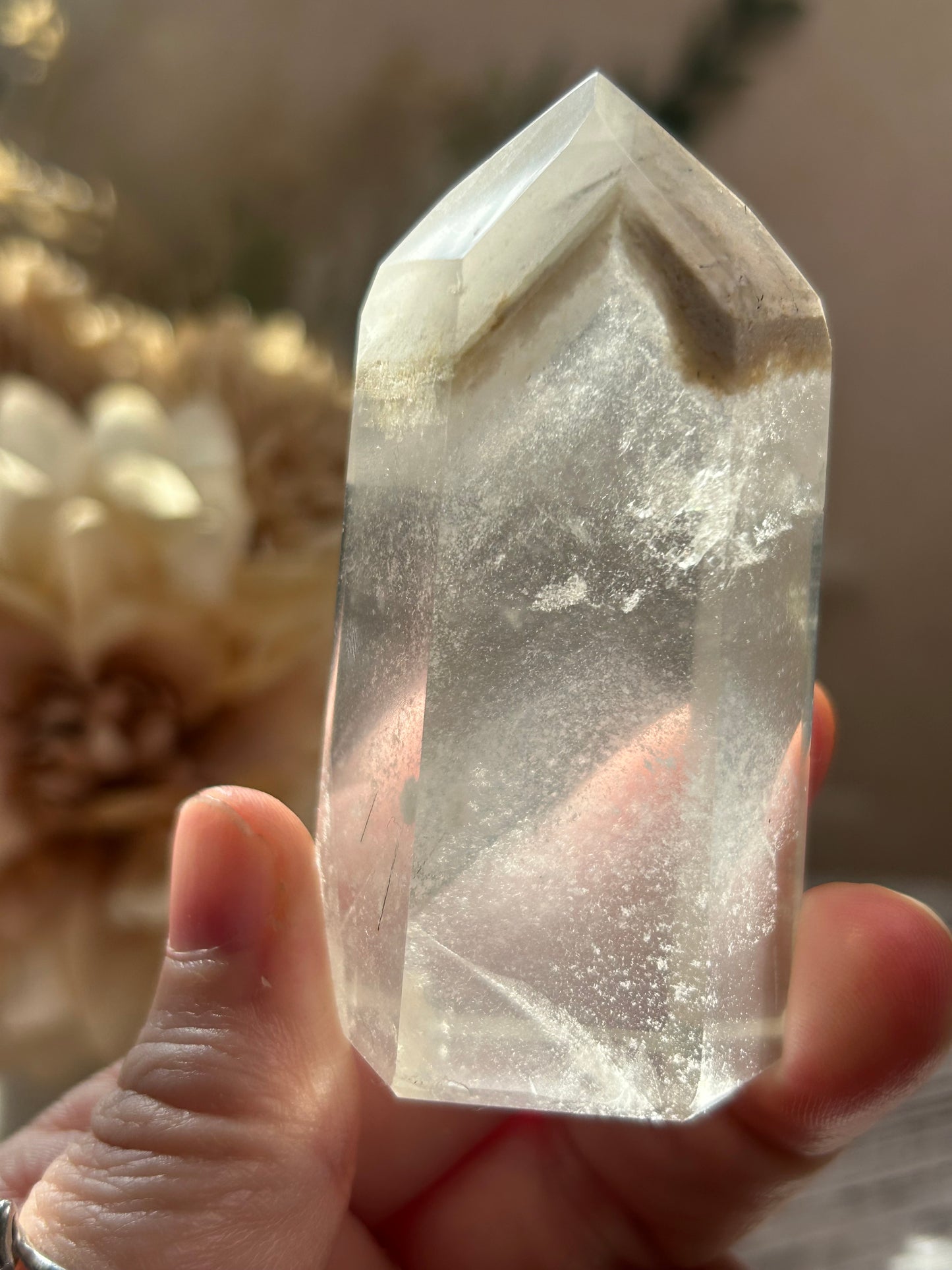 Clear crystal held in a hand with a blurred floral background