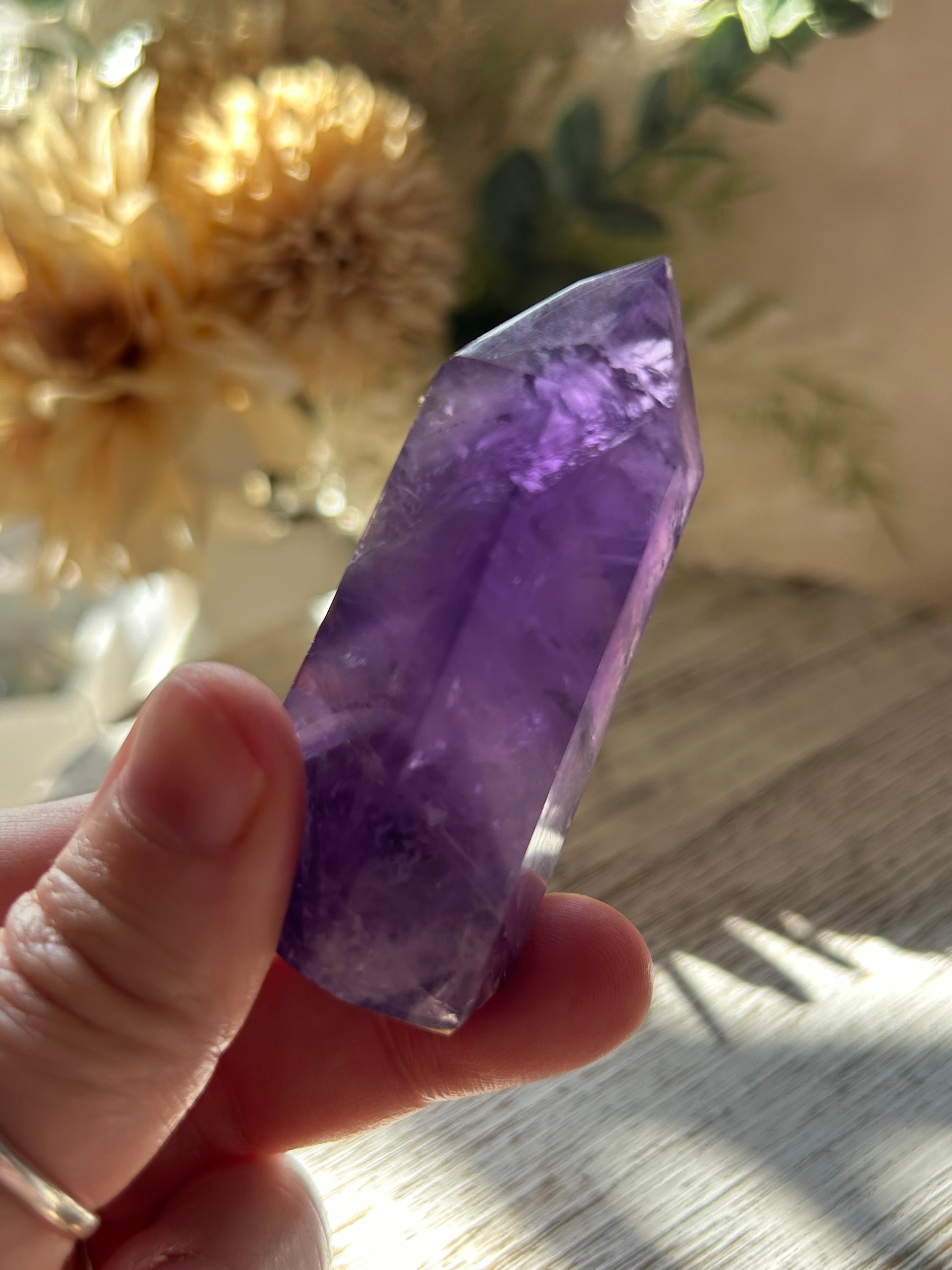 Hand holding a purple crystal with a blurred natural background