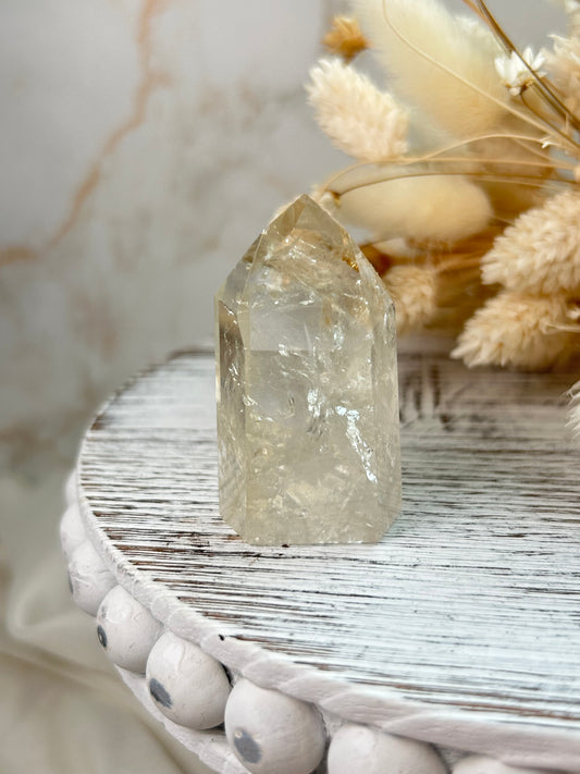 UV-reactive Amethyst tower with internal rainbows and vivid inclusions, polished point displayed on a rustic white wooden stand with dried flowers in the background