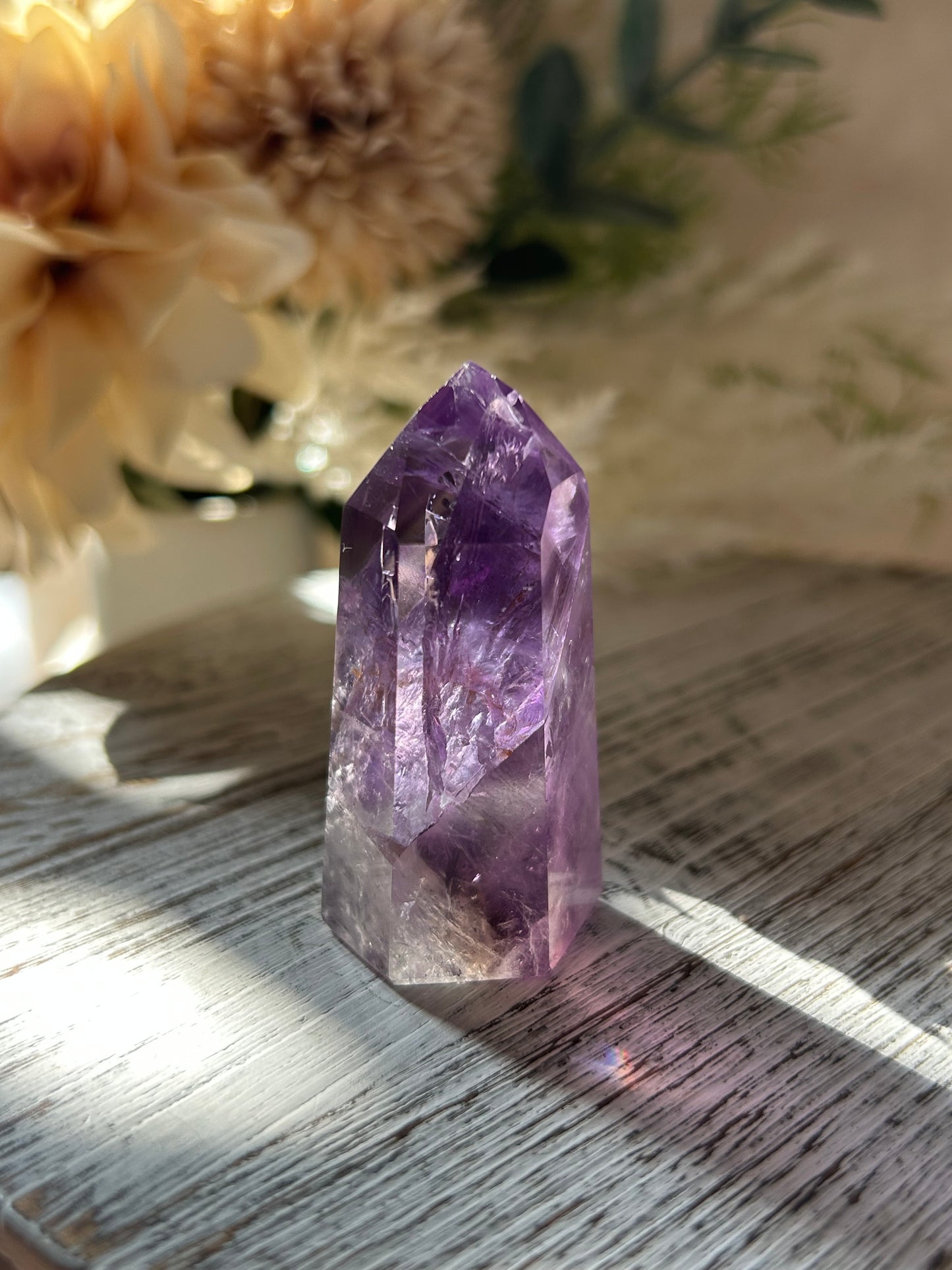 Amethyst crystal on a wooden surface with flowers in the background
