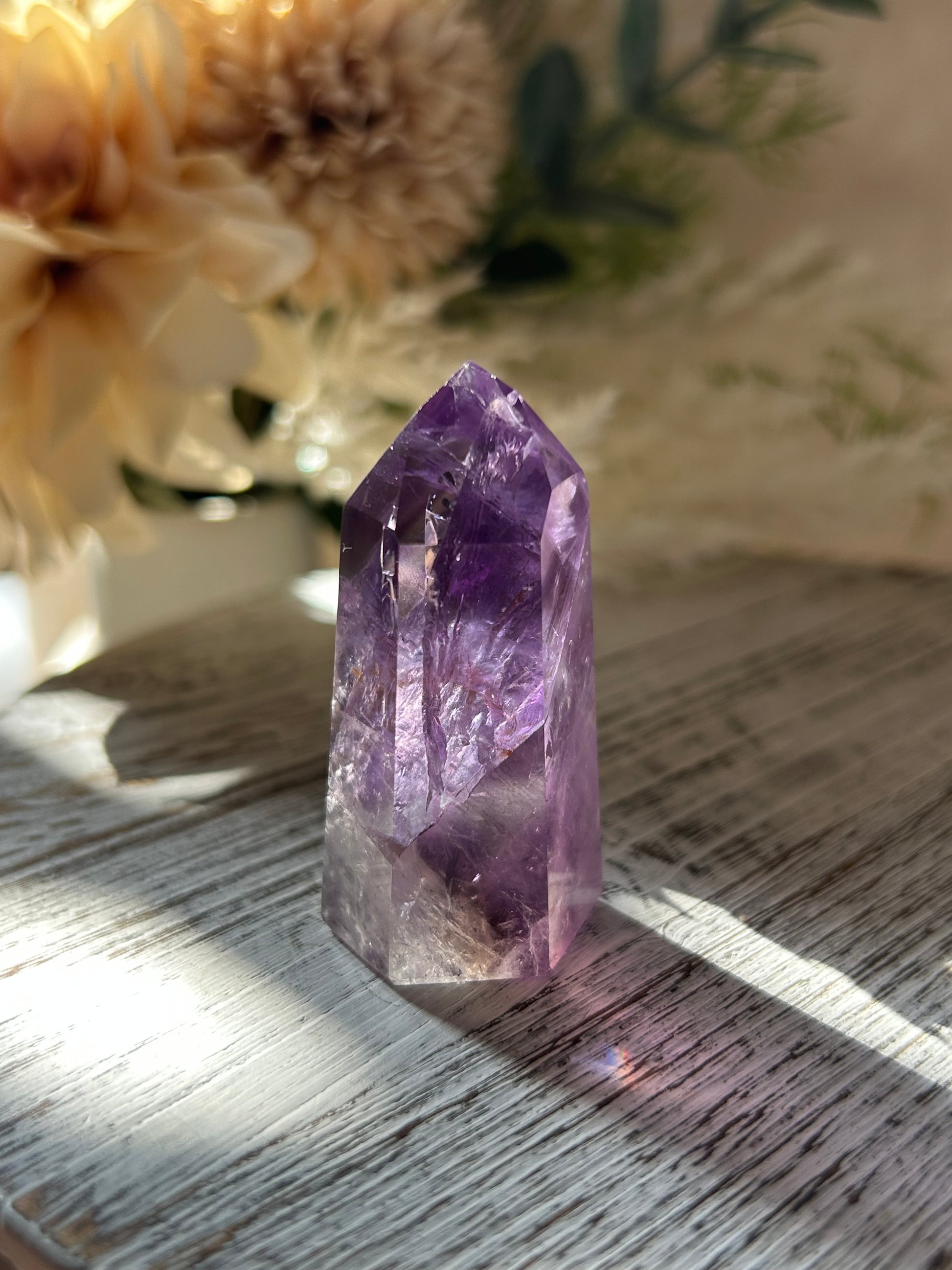 Amethyst crystal on a wooden surface with flowers in the background