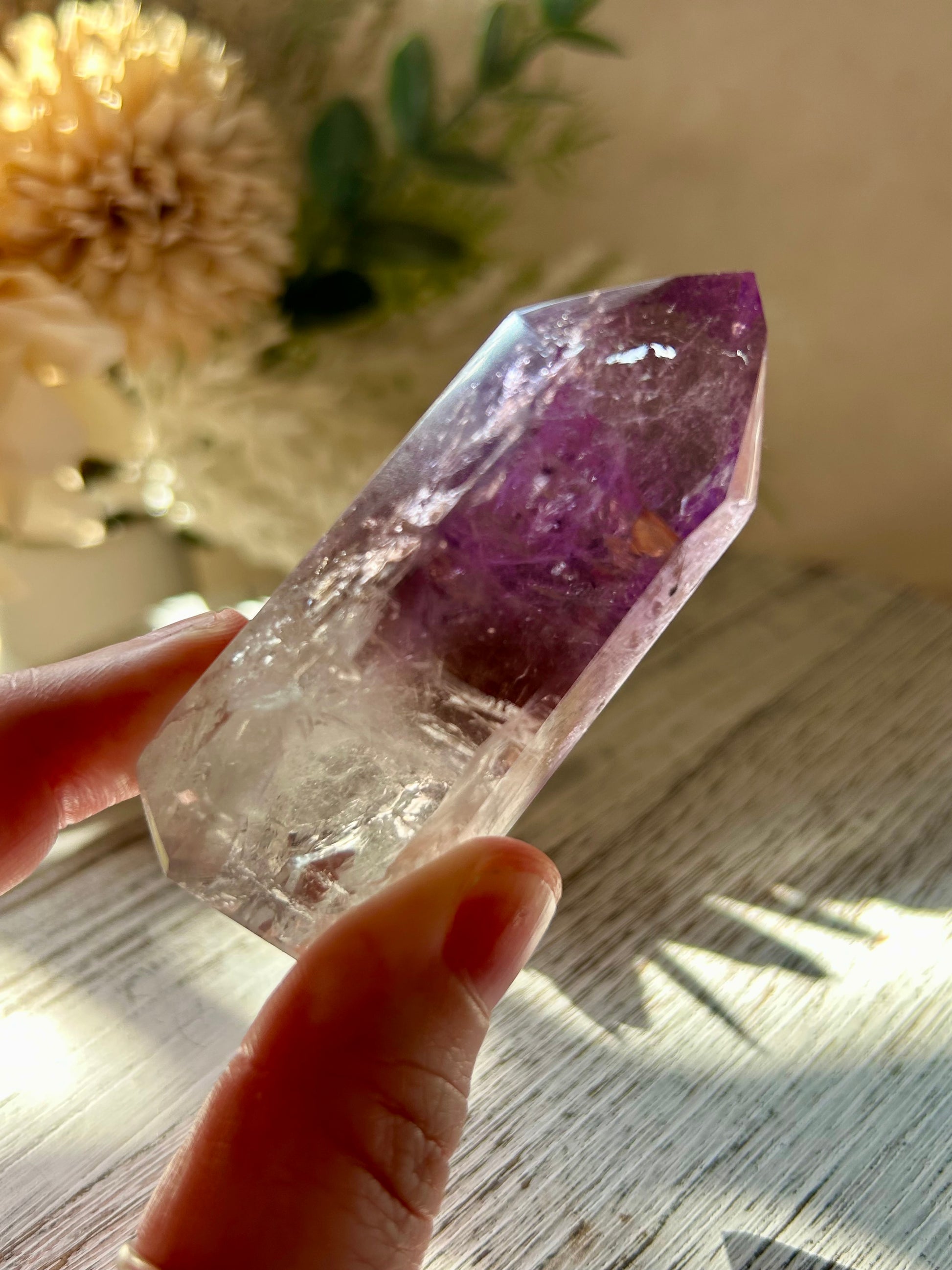 Amethyst crystal held by a hand on a wooden surface with decorative elements in the background