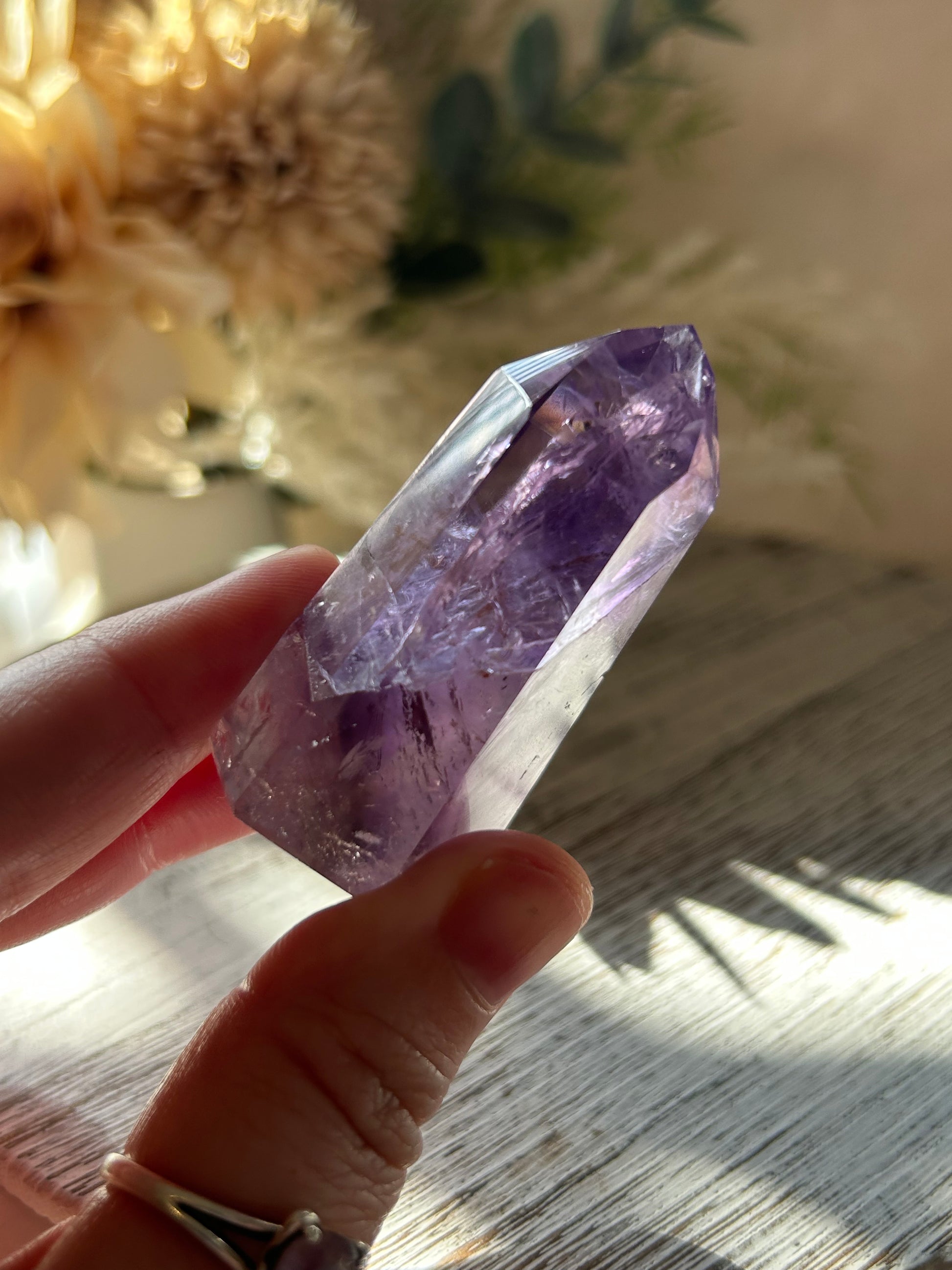 Hand holding a purple crystal with a blurred natural background