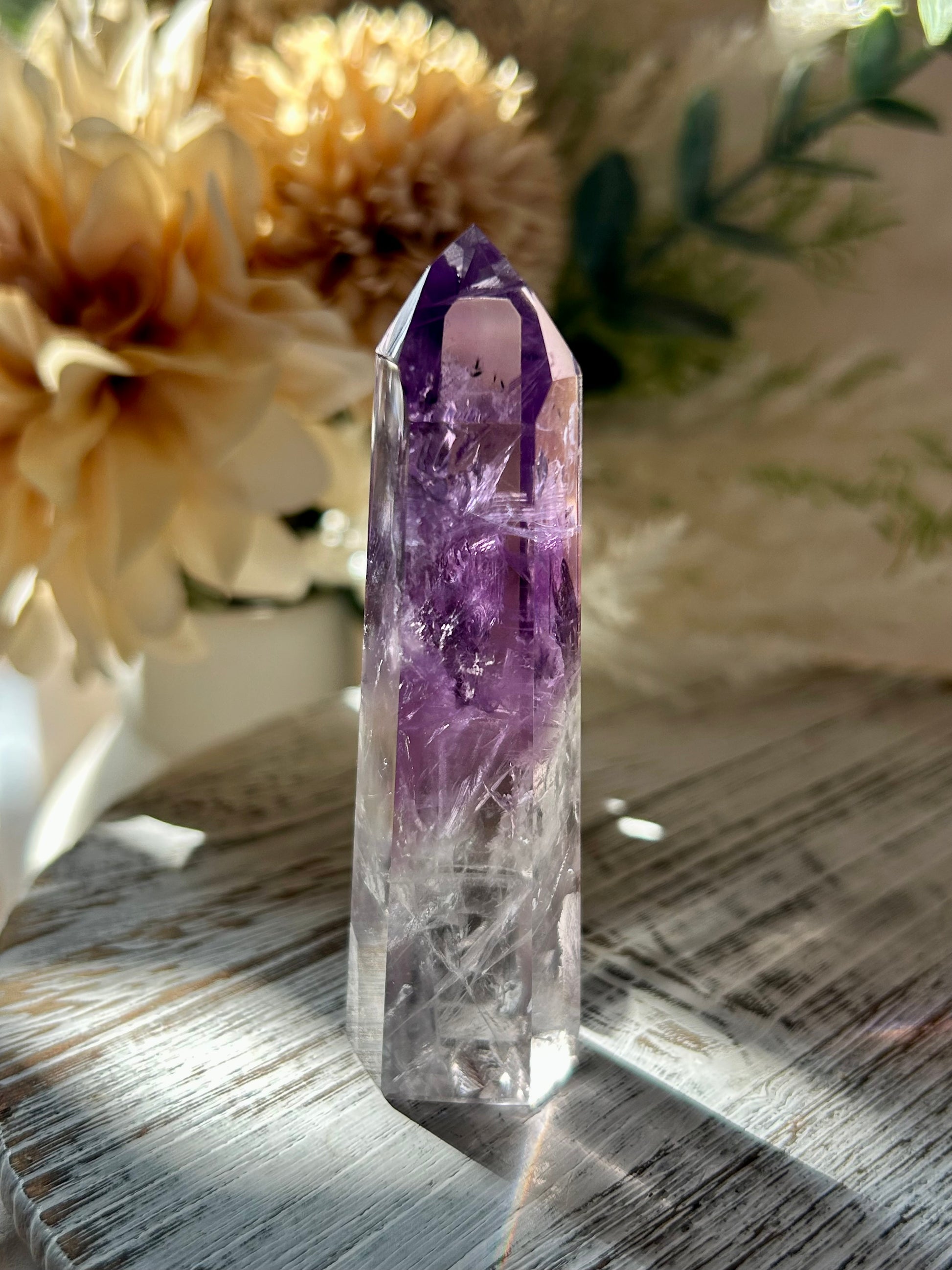 Amethyst crystal on a wooden surface with flowers in the background