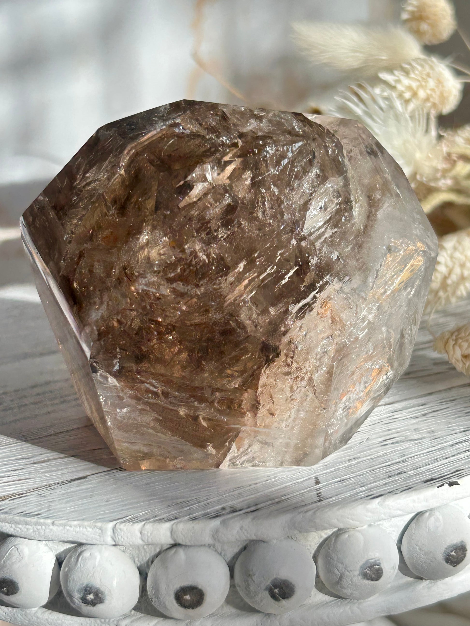 Golden Elestial Quartz crystal tower with visible layered terminations and internal inclusions, polished to a high shine. Photographed in warm natural light with soft cream dried florals in the background.