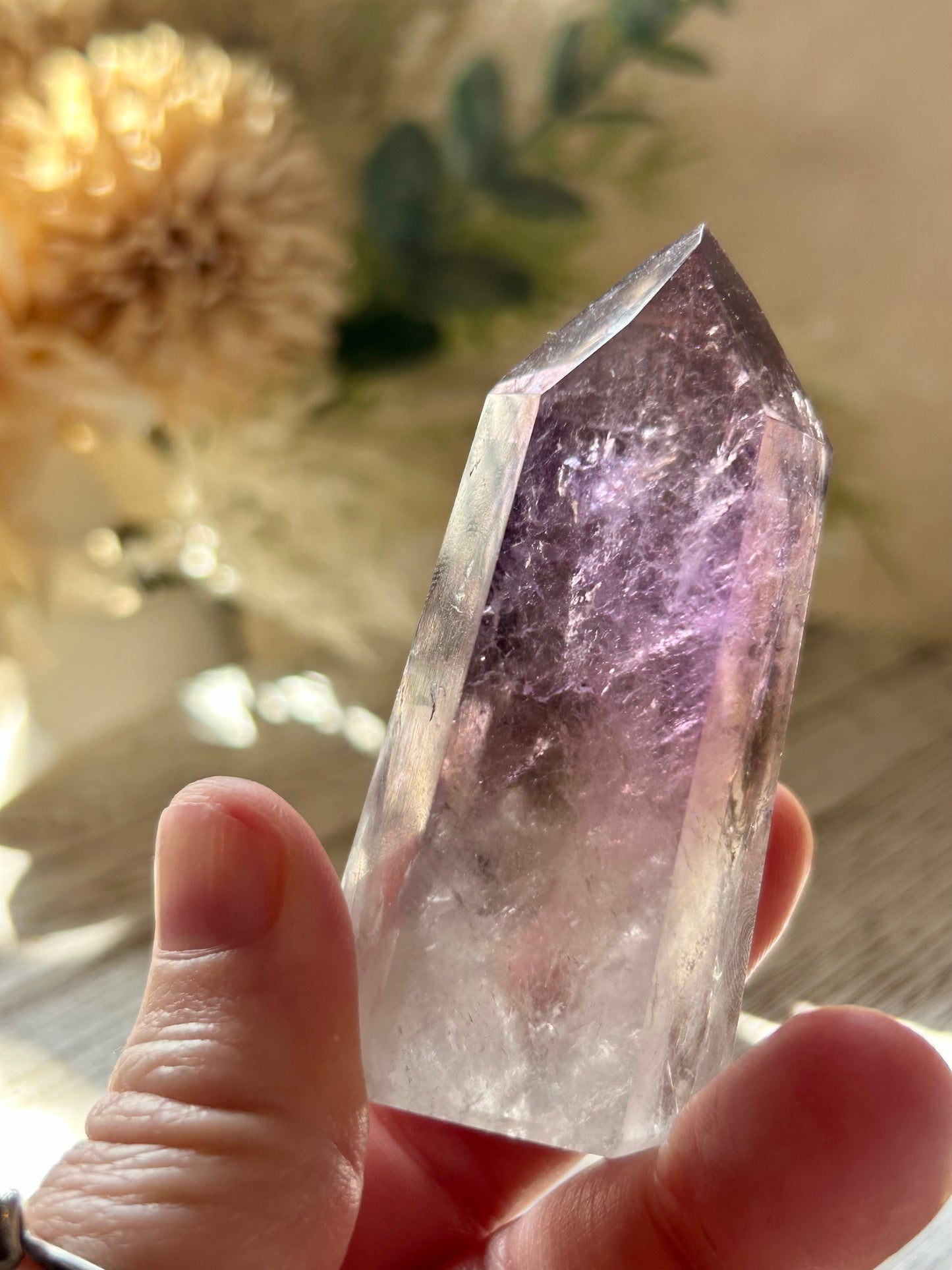Amethyst crystal held in a hand with a blurred natural background