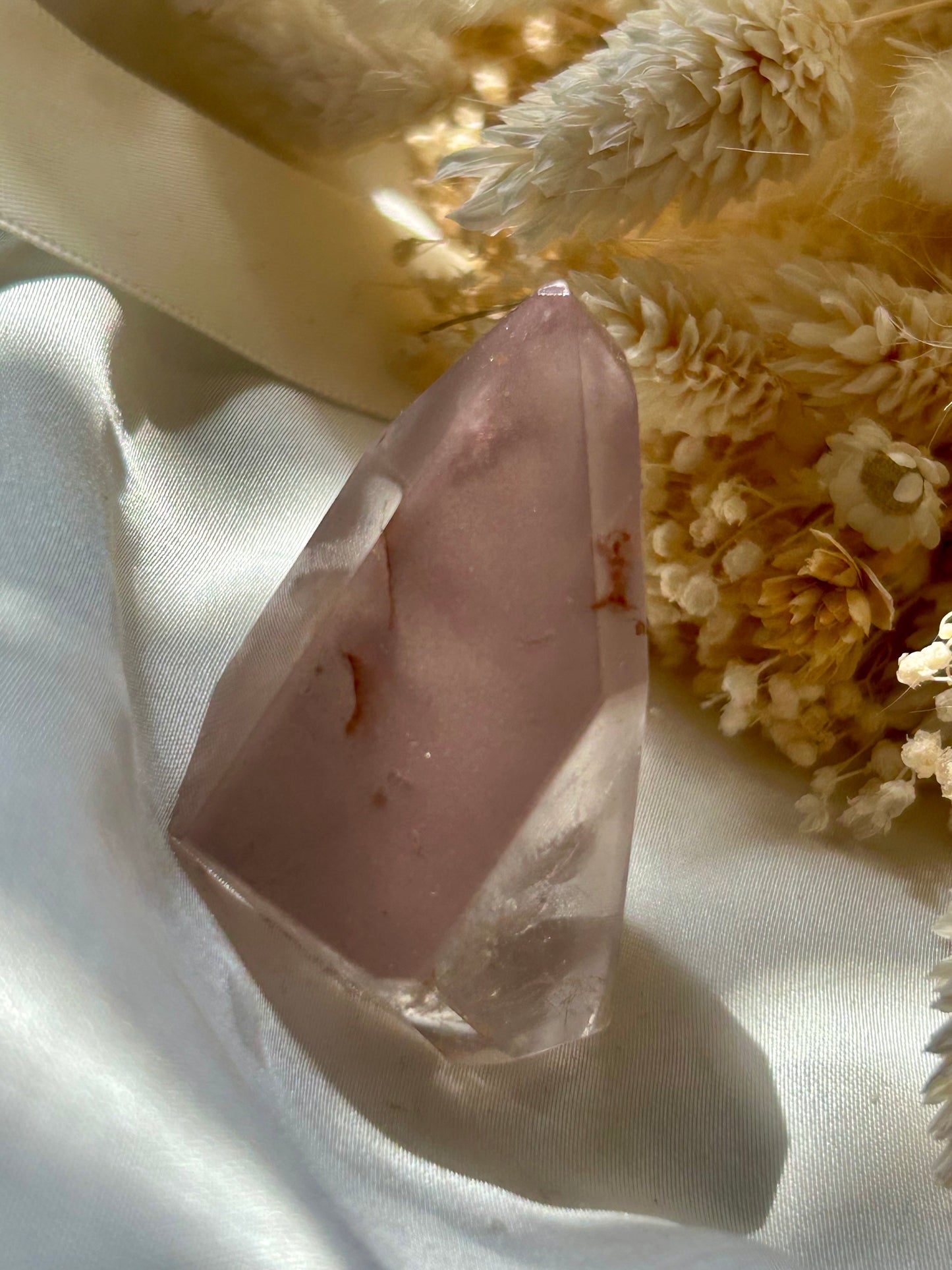 Each pink lithium piece is sitting in the sun on an ivory satin background with cream dried flowers in the background.

