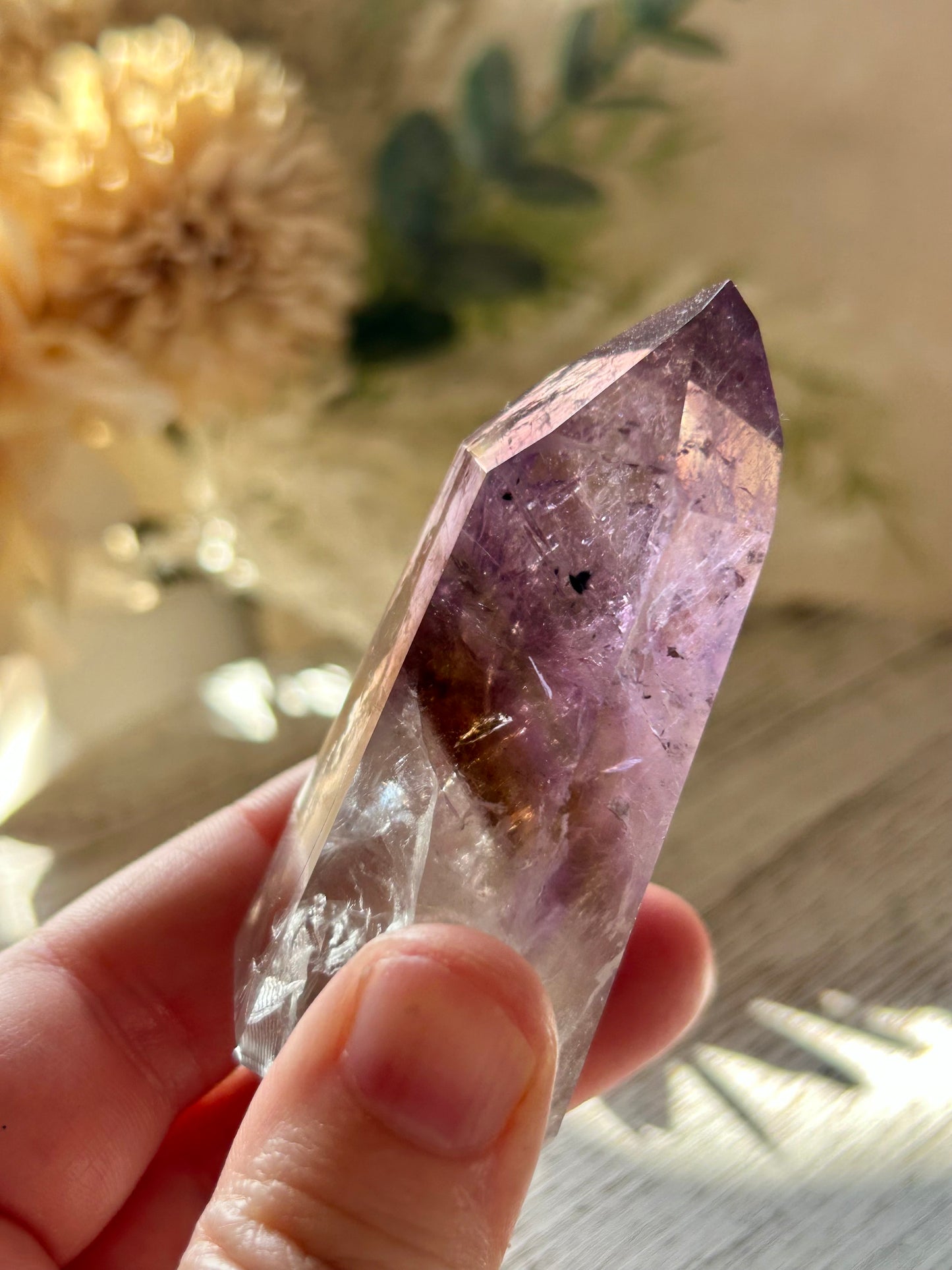 Amethyst crystal held in a hand with a blurred natural background