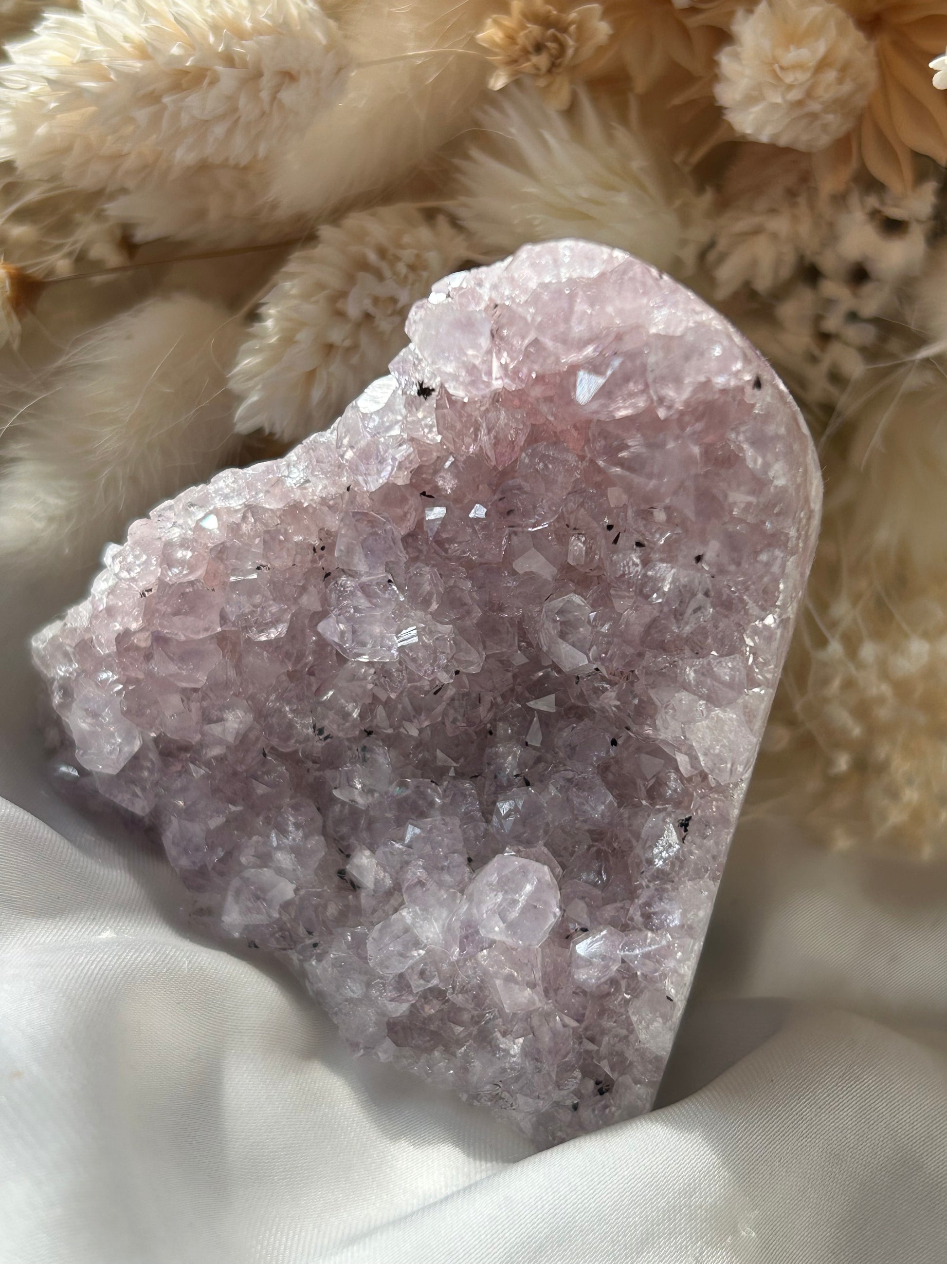 Lavender Amethyst crystal heart with sparkly sugar-like coating, soft pink-purple hue, displayed on white silk with dried florals