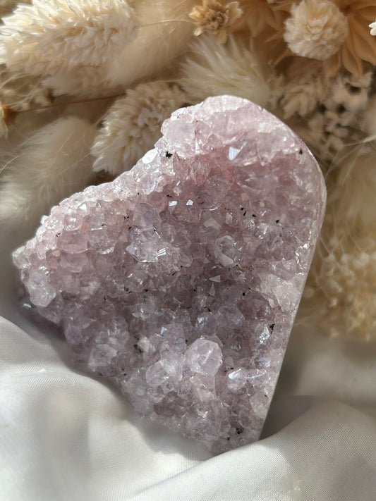 Lavender Amethyst crystal heart with sparkly sugar-like coating, soft pink-purple hue, displayed on white silk with dried florals