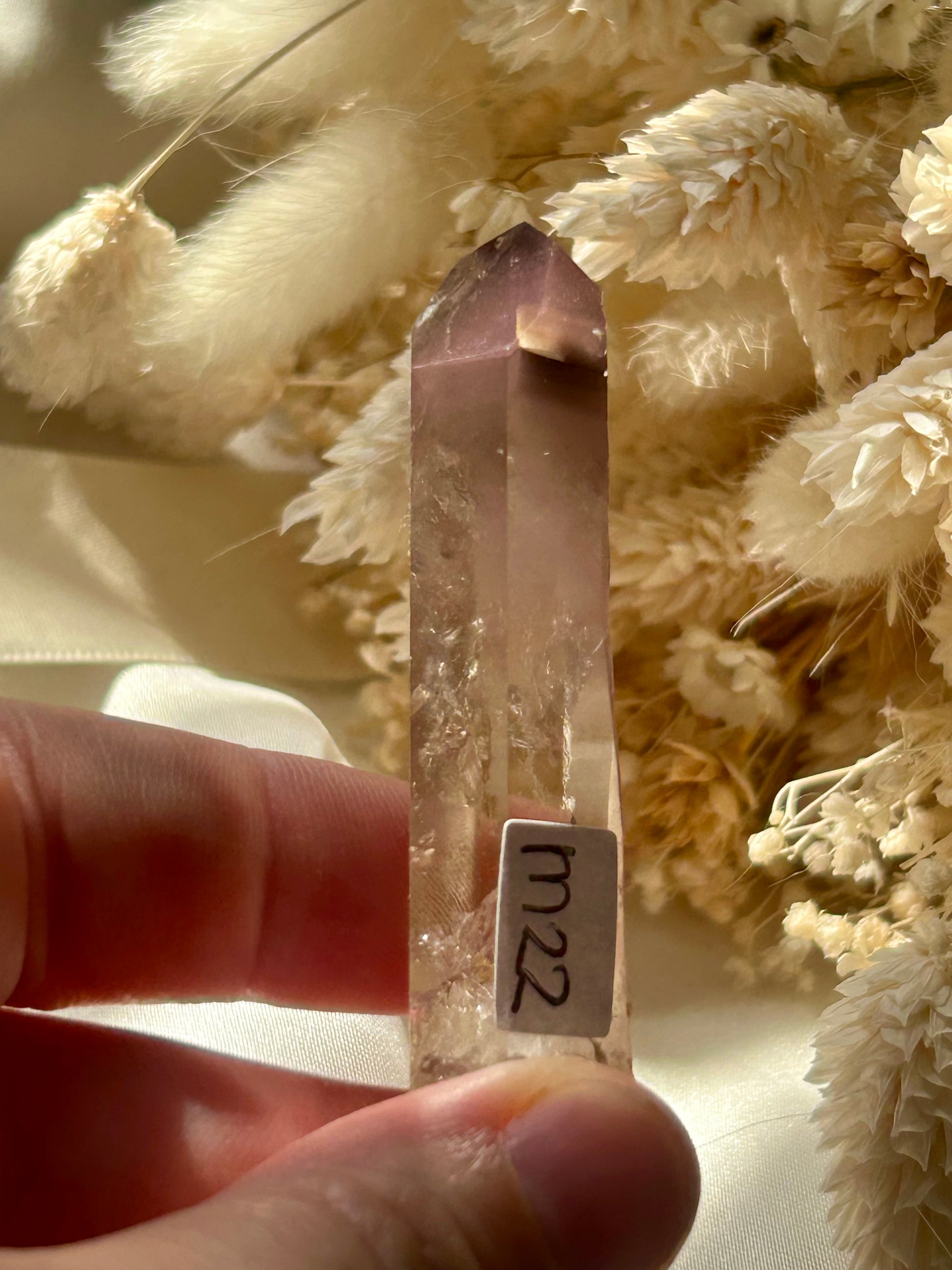 Each pink lithium piece is sitting in the sun on an ivory satin background with cream dried flowers in the background.
