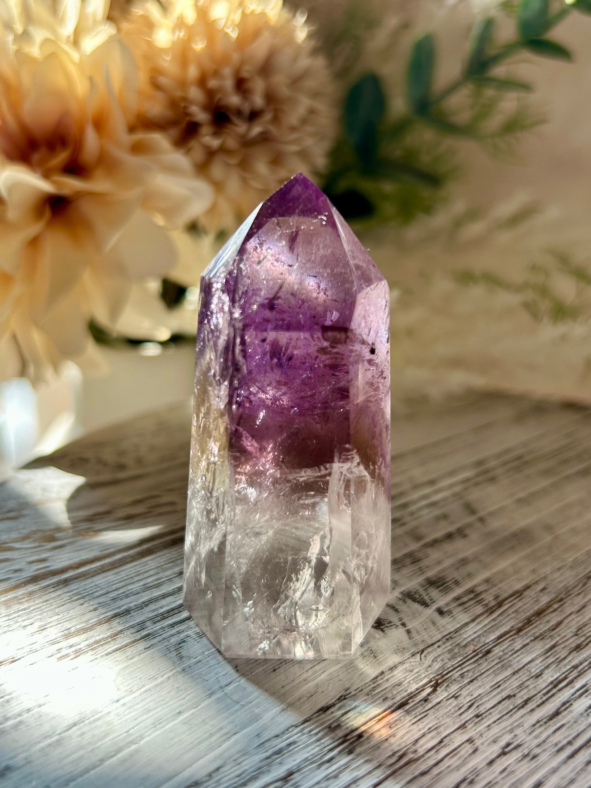 Amethyst crystal on a wooden surface with flowers in the background