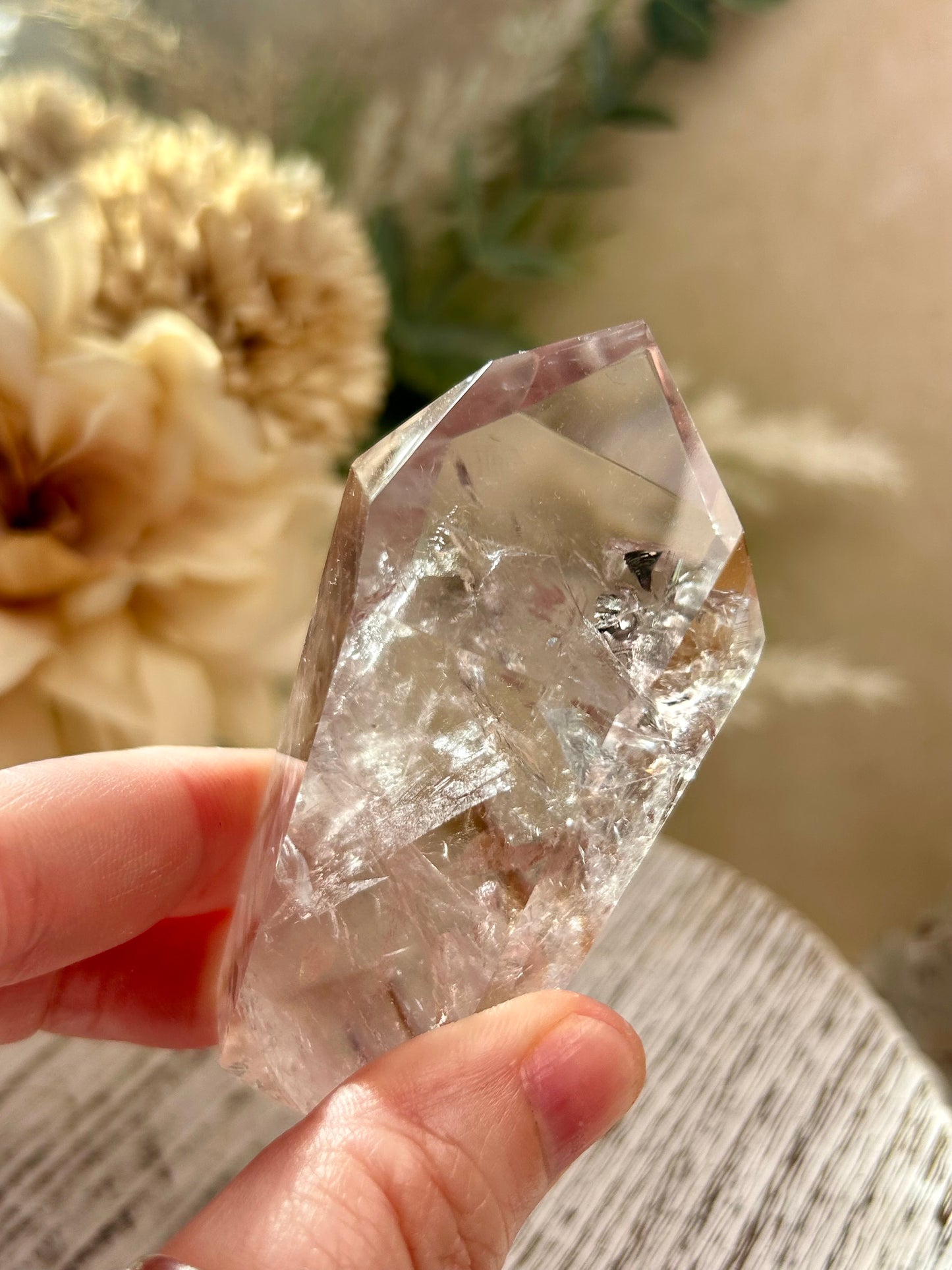 Clear crystal held by a hand with a blurred floral background
