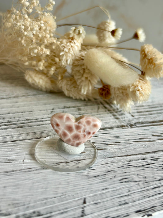 Soft coral-toned pink natrolite heart cut crystal displaying subtle internal inclusions and shine, in warm daylight.