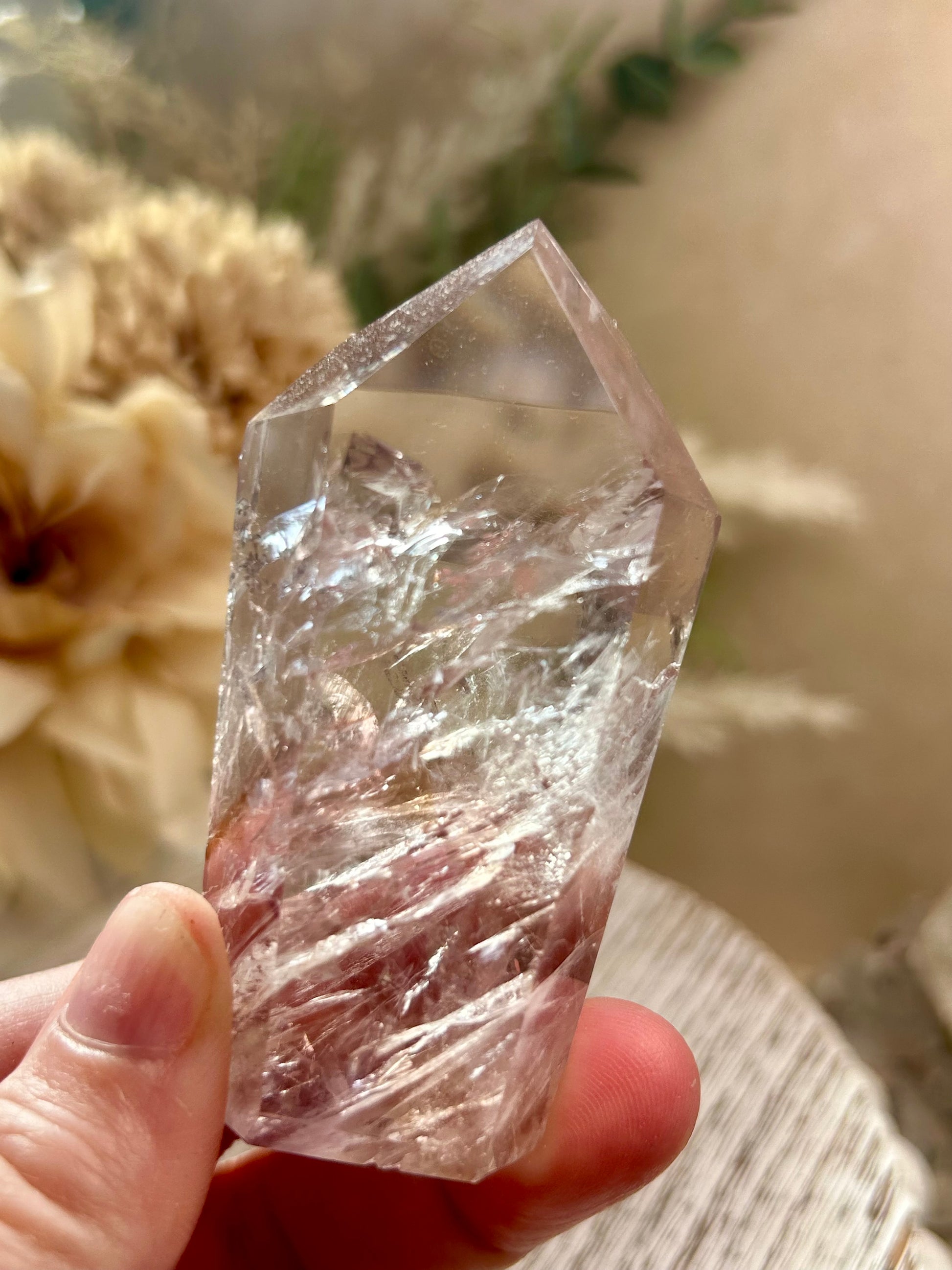 Clear crystal held in a hand with a blurred natural background