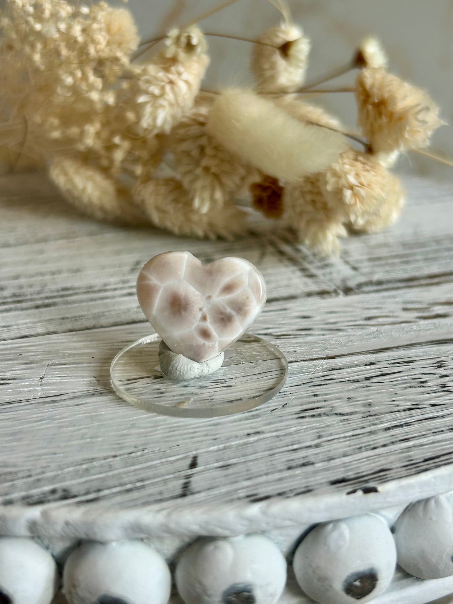 Soft coral-toned pink natrolite heart cut crystal displaying subtle internal inclusions and shine, in warm daylight.