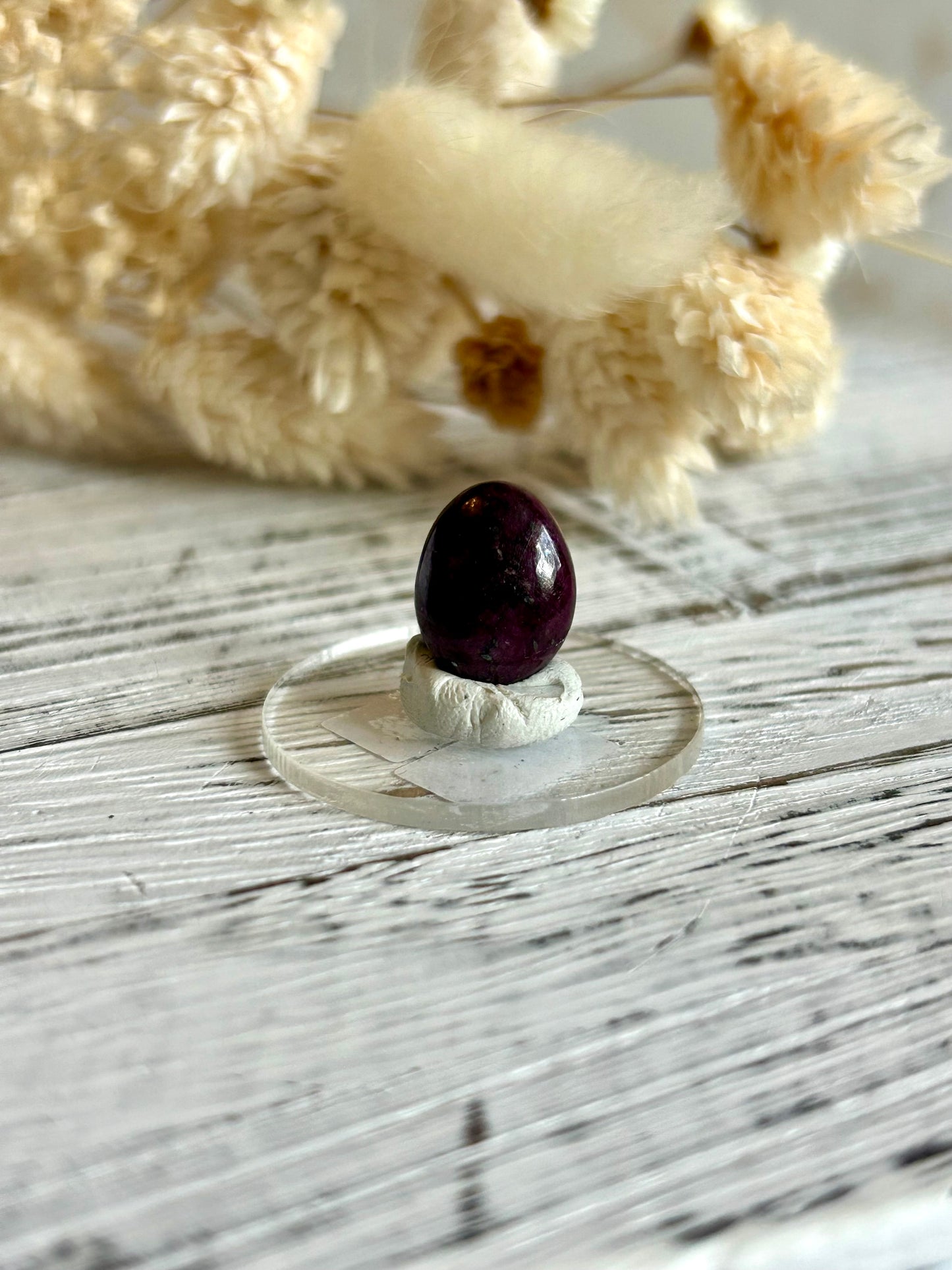 Polished natural Ruby cabochon with deep magenta-red tones, displayed against dried florals in soft natural light
