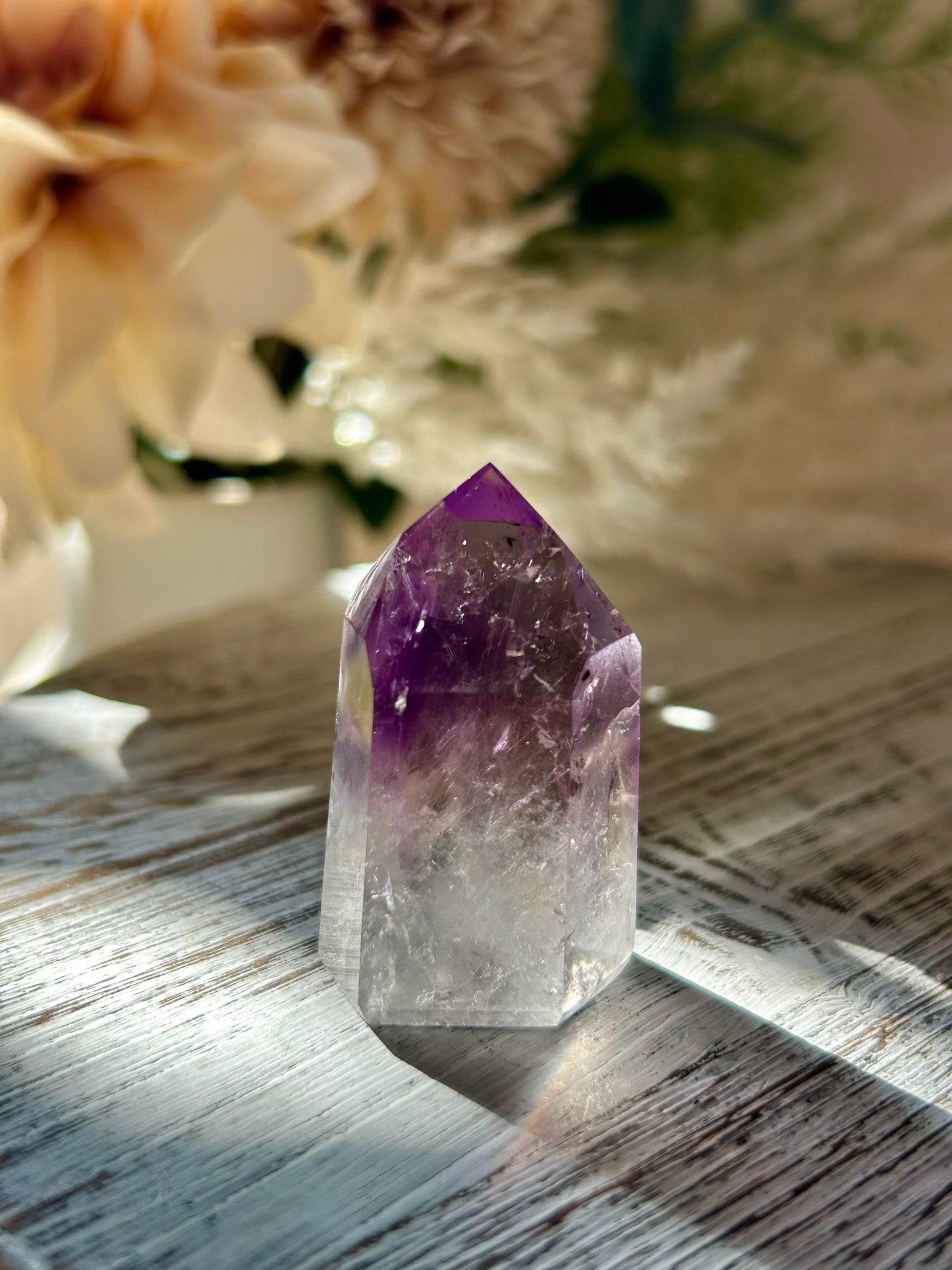 Amethyst crystal on a wooden surface with blurred flowers in the background