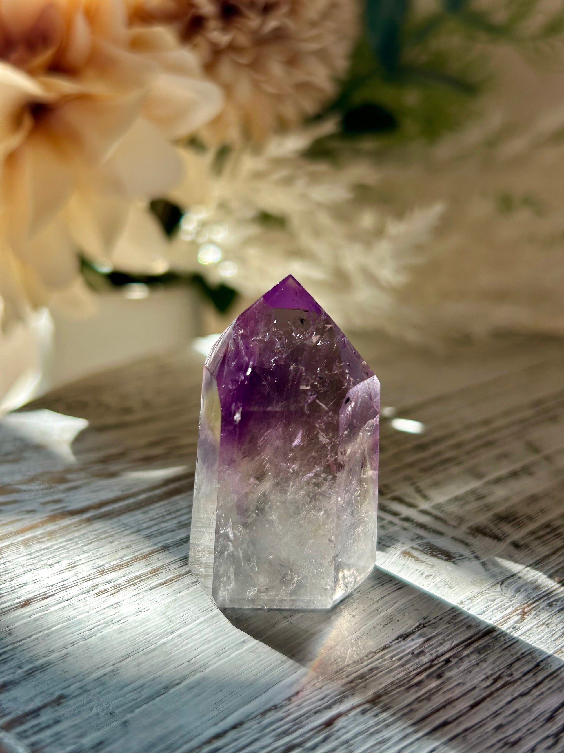 Amethyst crystal on a wooden surface with blurred flowers in the background