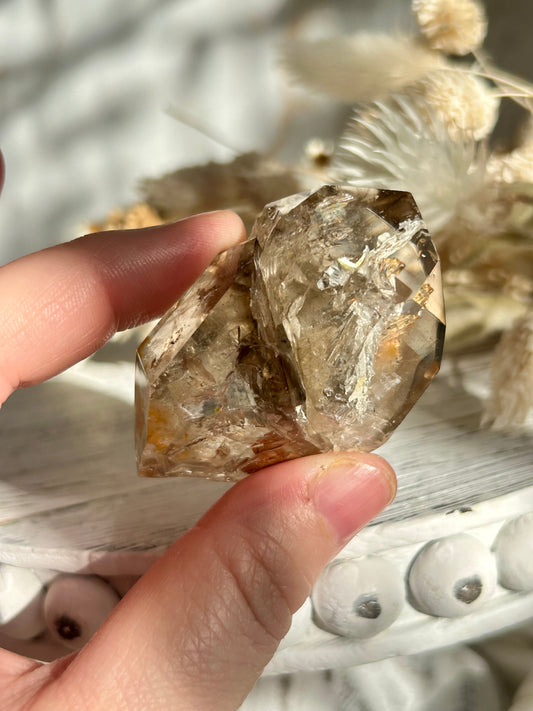 Golden Elestial Quartz crystal tower with visible layered terminations and internal inclusions, polished to a high shine. Photographed in warm natural light with soft cream dried florals in the background.