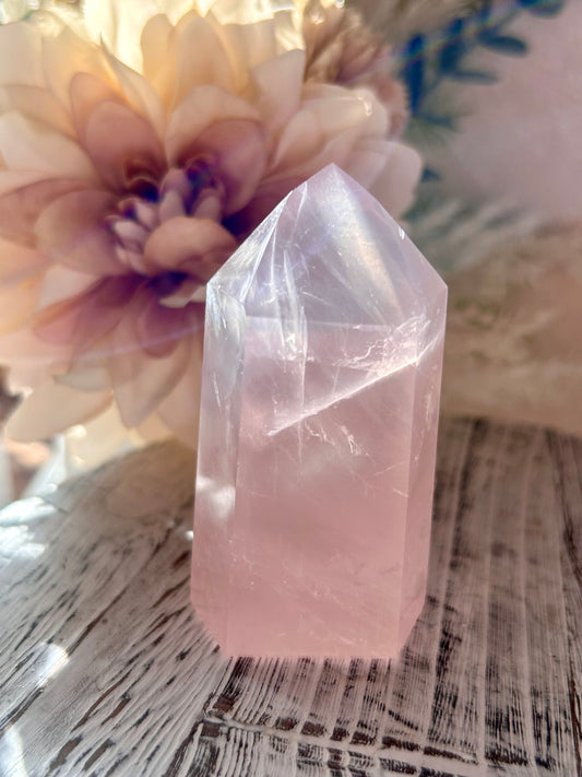 Crystal tower with a soft pink hue on a textured surface with flowers in the background