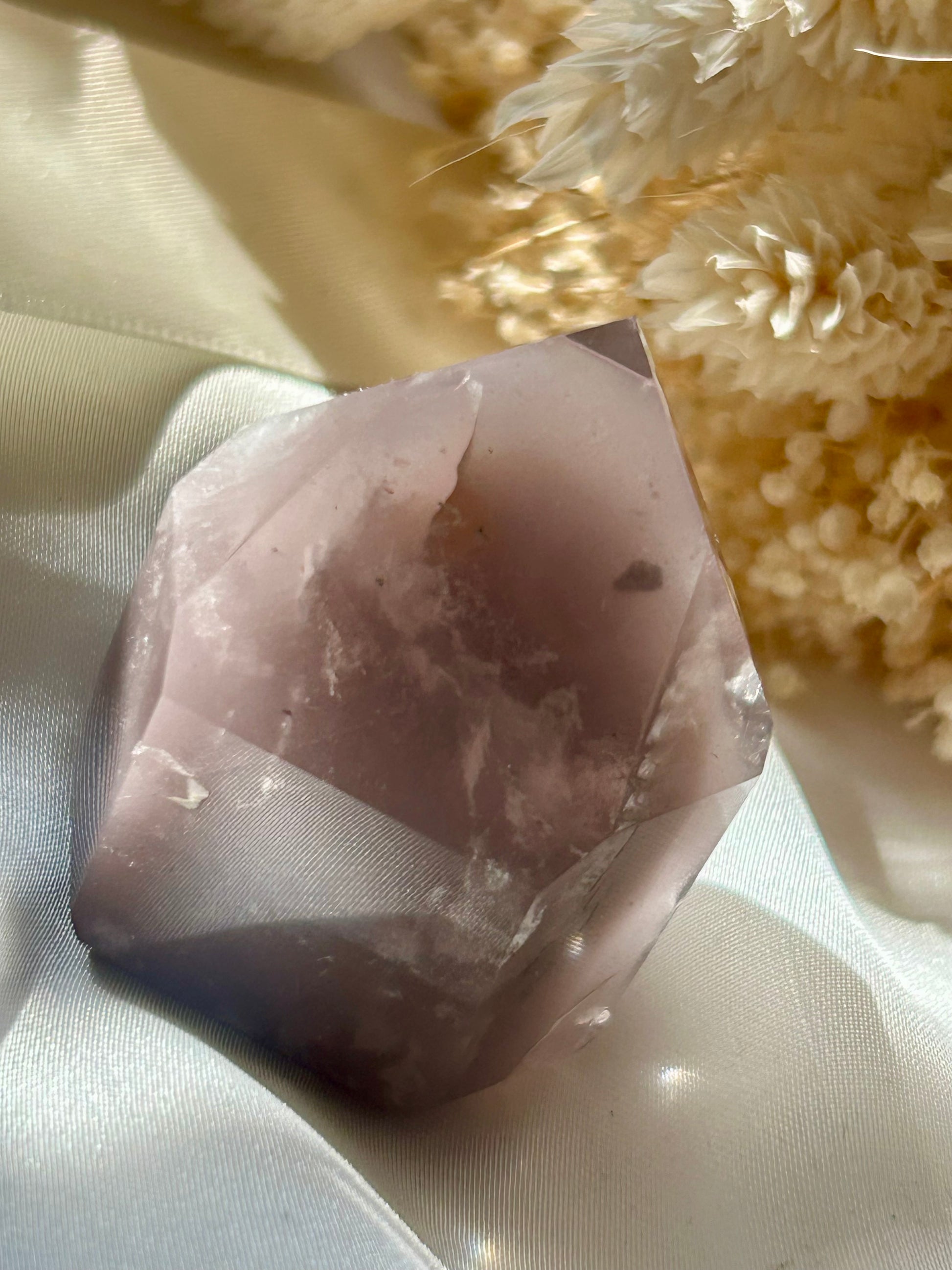 Each pink lithium piece is sitting in the sun on an ivory satin background with cream dried flowers in the background.
