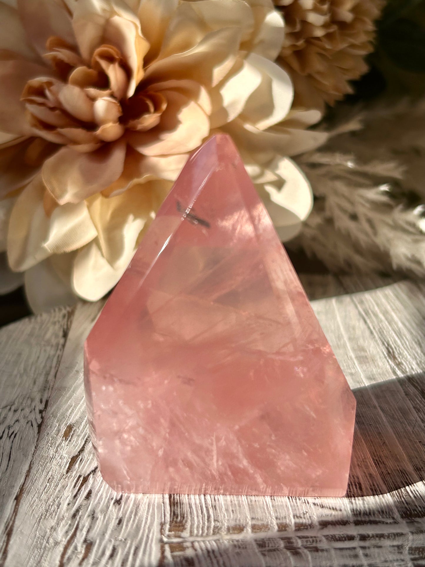 A pink quartz crystal pyramid stand on a rustic wooden surface, with dried flowers in the background.