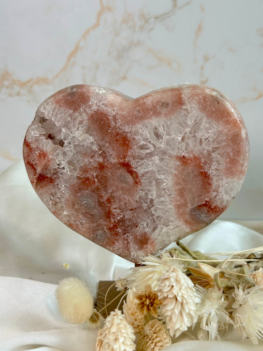 Pink Amethyst heart with blush rose and peach tones, sparkling druzy patches, and crystal flowering. Displayed on white satin with soft dried florals.