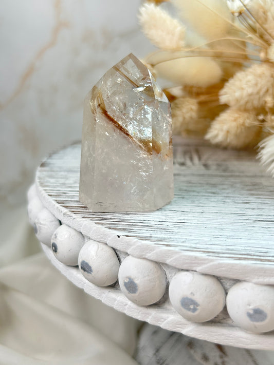 UV-reactive Amethyst tower with internal rainbows and vivid inclusions, polished point displayed on a rustic white wooden stand with dried flowers in the background