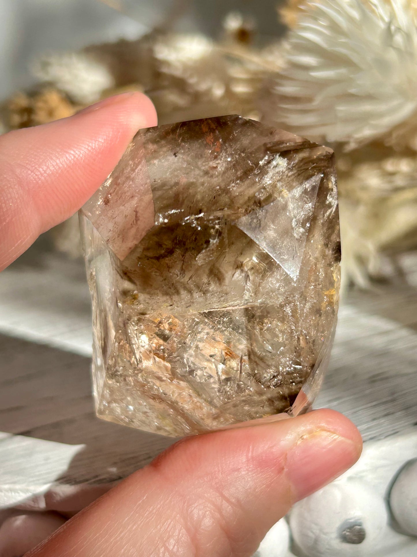 Golden Elestial Quartz crystal tower with visible layered terminations and internal inclusions, polished to a high shine. Photographed in warm natural light with soft cream dried florals in the background.