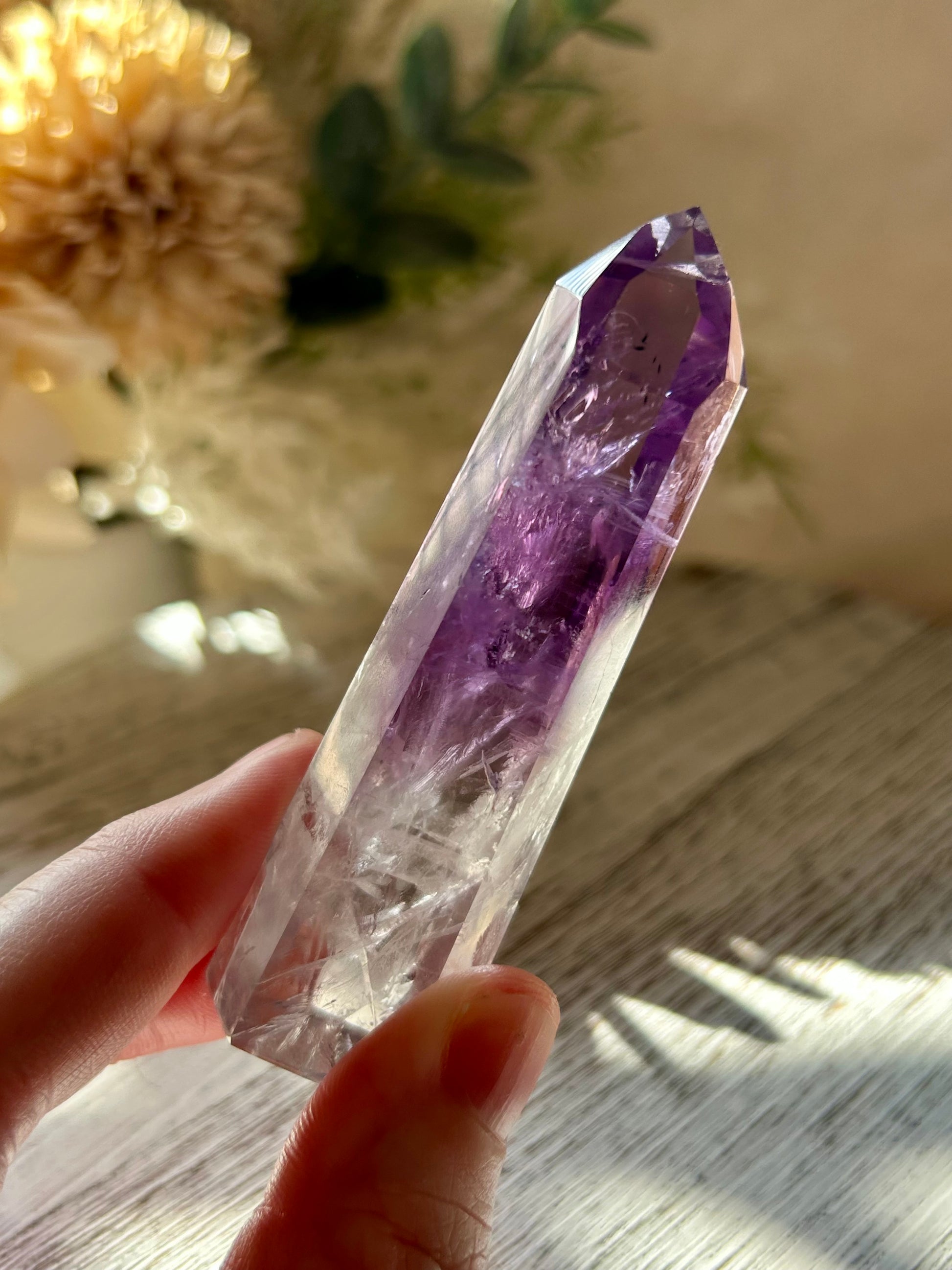 Amethyst crystal held by a hand on a wooden surface with a blurred background