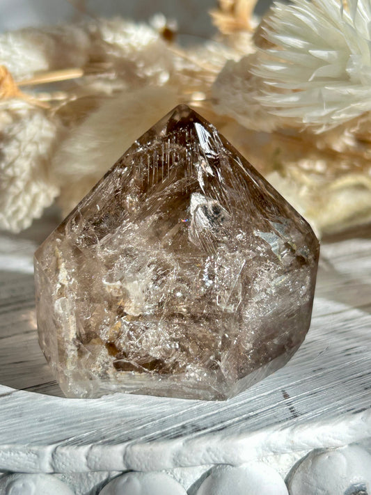 Golden Elestial Quartz crystal tower with visible layered terminations and internal inclusions, polished to a high shine. Photographed in warm natural light with soft cream dried florals in the background.