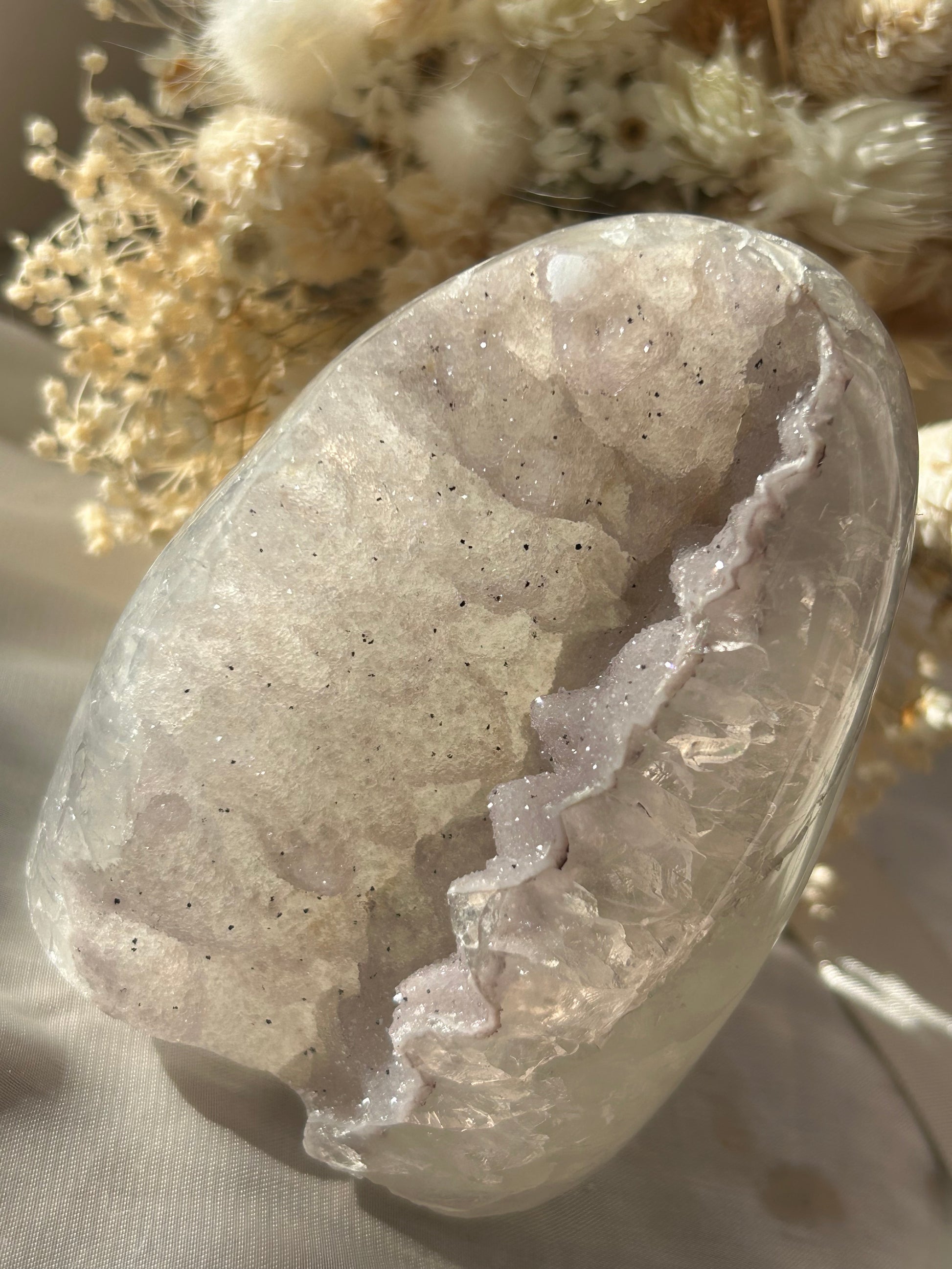 Polished white sugar amethyst geode with fine druzy crystals from Uruguay, softly sparkling in natural sunlight with floral background