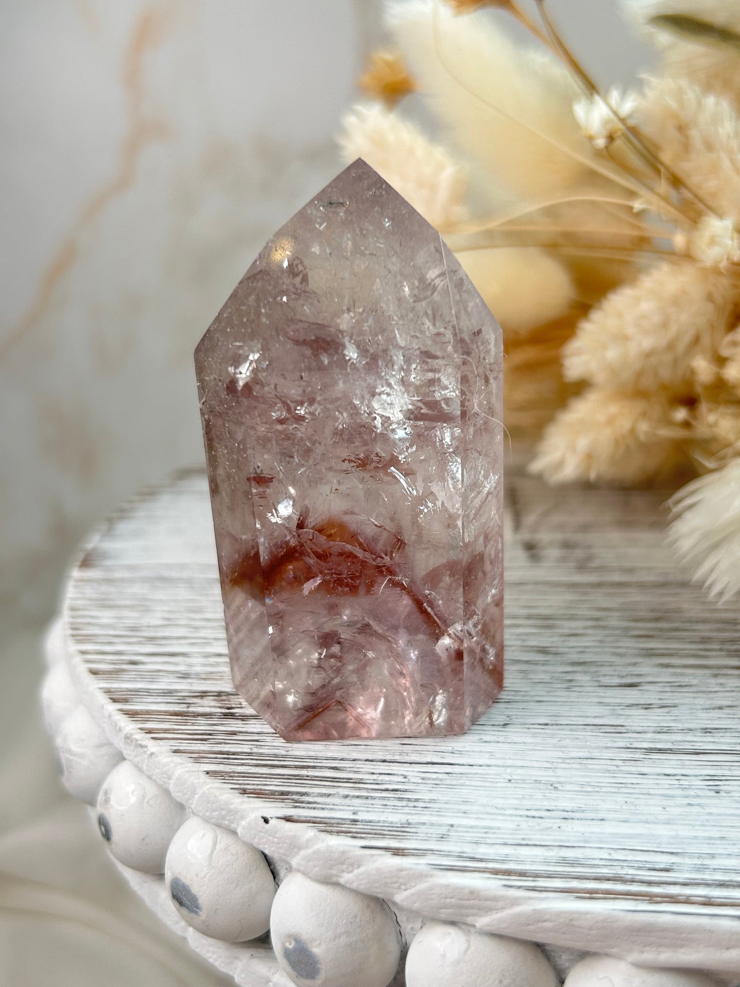 UV-reactive Amethyst tower with internal rainbows and vivid inclusions, polished point displayed on a rustic white wooden stand with dried flowers in the background