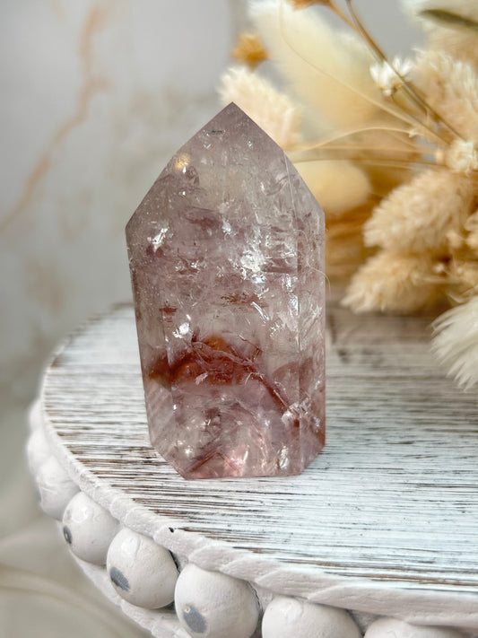 UV-reactive Amethyst tower with internal rainbows and vivid inclusions, polished point displayed on a rustic white wooden stand with dried flowers in the background