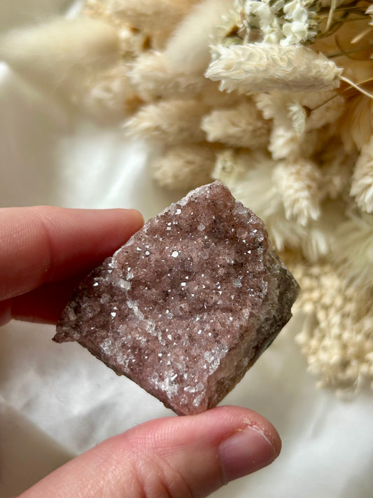 Small druzy rainbow sugar geode clusters with pastel tones and glittering crystal surfaces, displayed on ivory silk with cream dried flowers in the background.