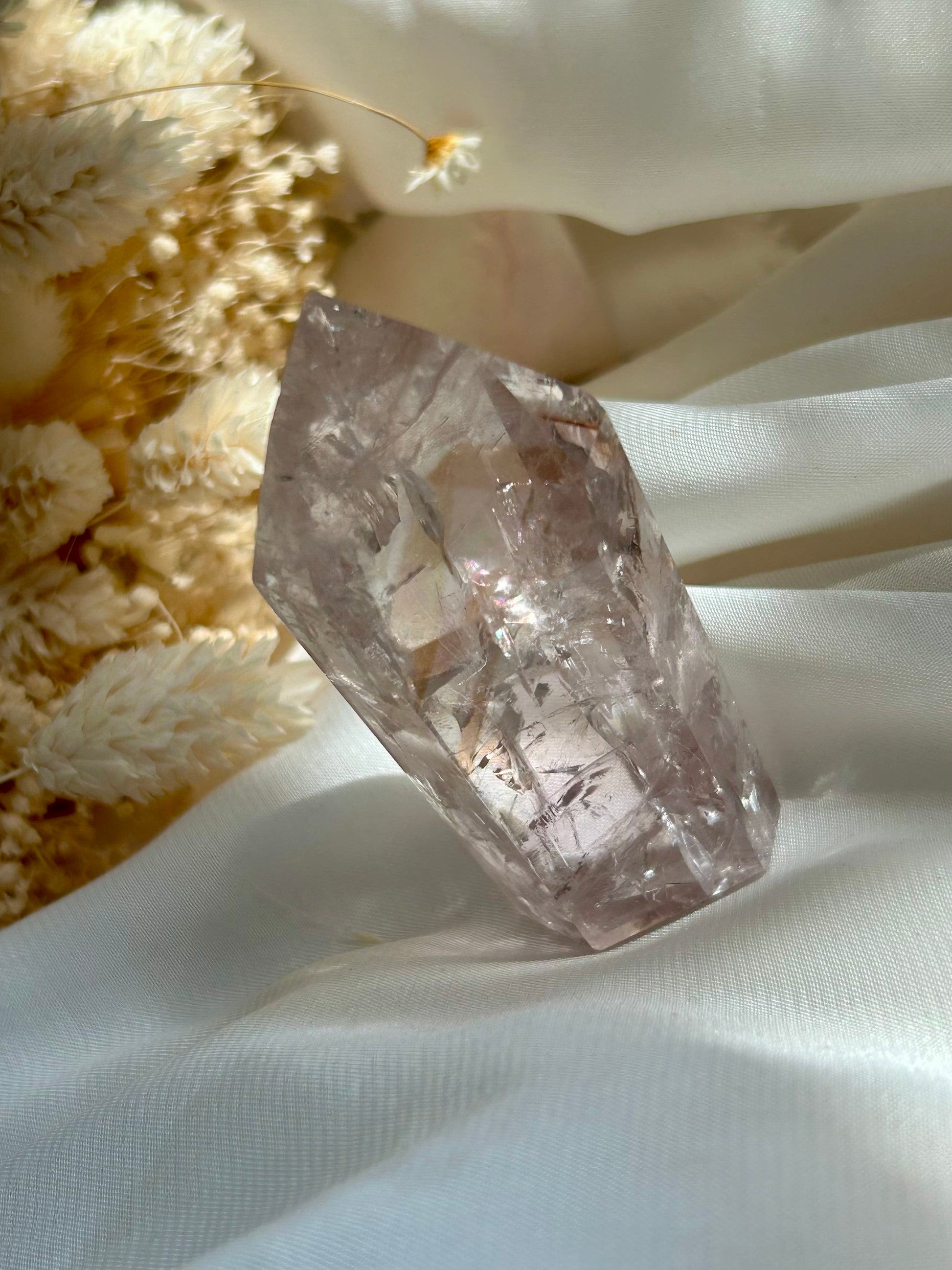 UV reactive Amethyst with golden rod-like inclusions — photographed on ivory satin with cream dried flowers. Gentle crystal for transformation, clarity, and spiritual alignment.