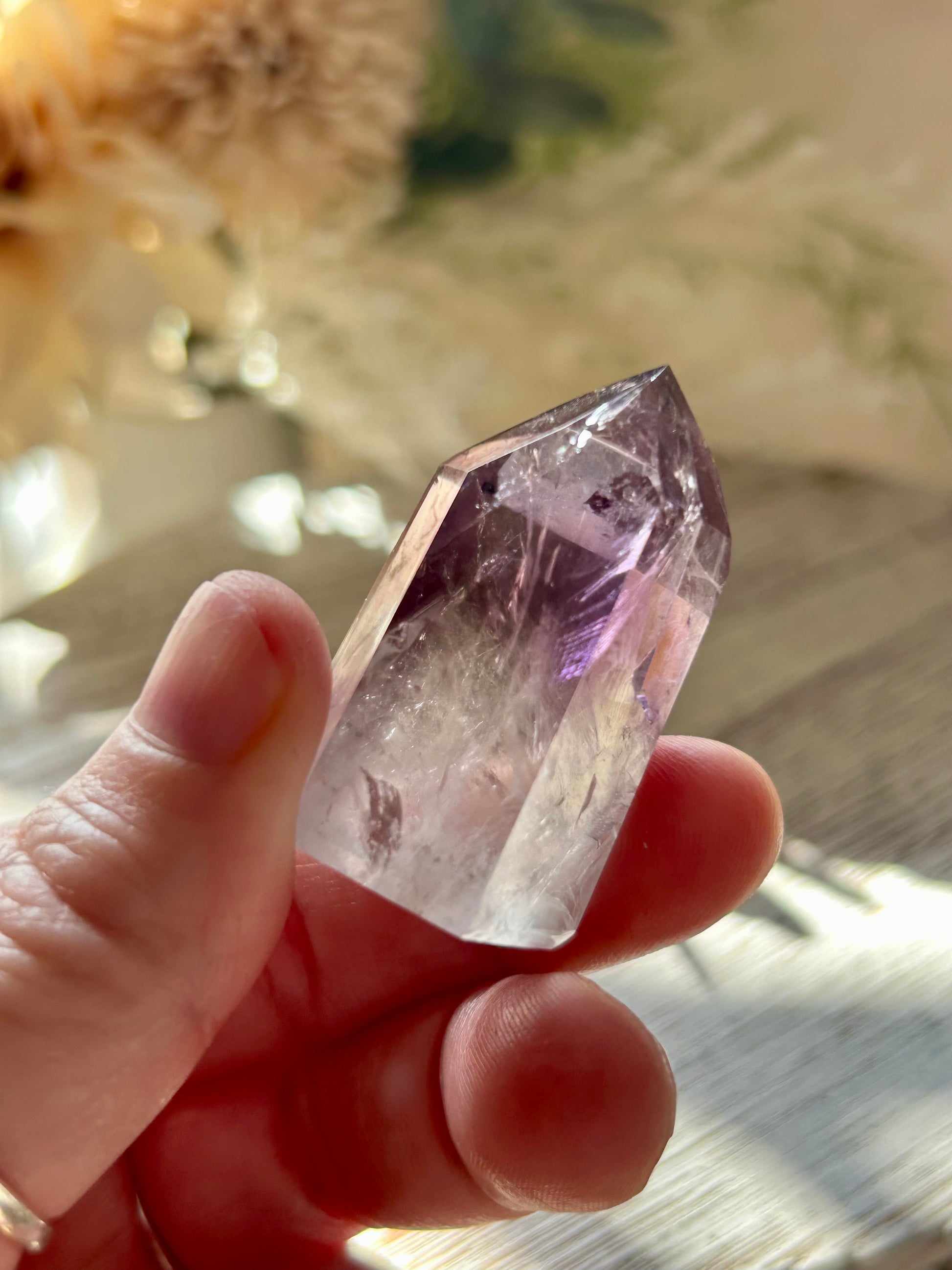 Hand holding a clear crystal with purple undertones against a blurred natural background