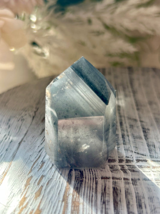 A natural pointed crystal cluster, likely a quartz point, with layered gray and blue bands, resting on a rustic white-washed wooden surface.