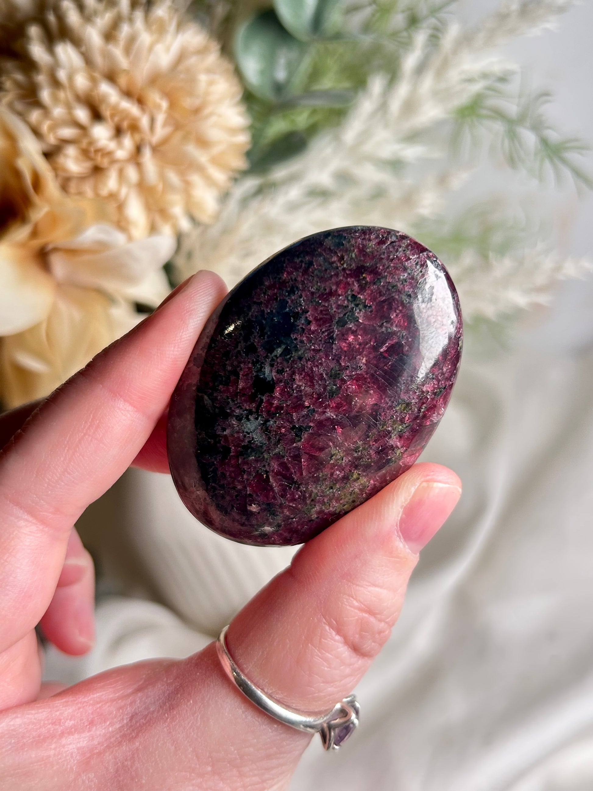 Polished deep red garnet palm stone with rich wine tones and smooth finish, photographed in soft neutral setting.