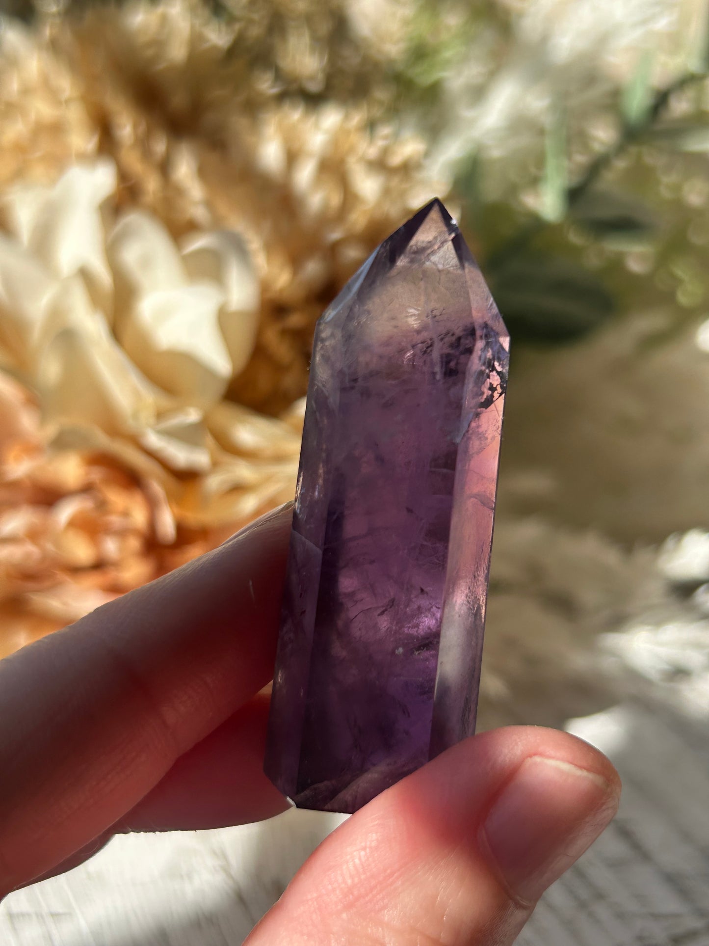 A hand holding a polished purple amethyst crystal point against a blurred outdoor background.